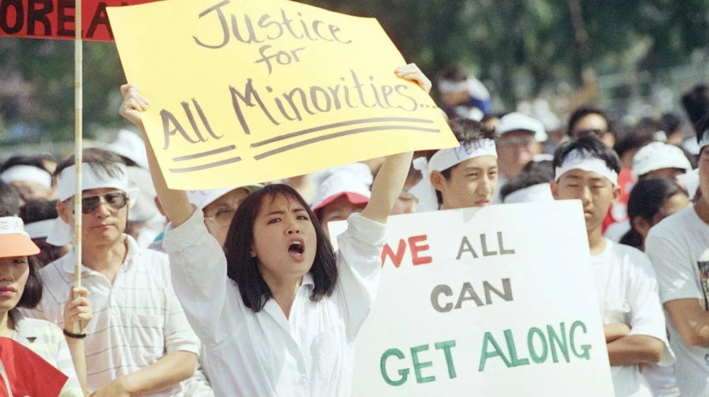 Crowd of people in outdoor gathering. People hold signs calling for healing between the Korean and African American community.