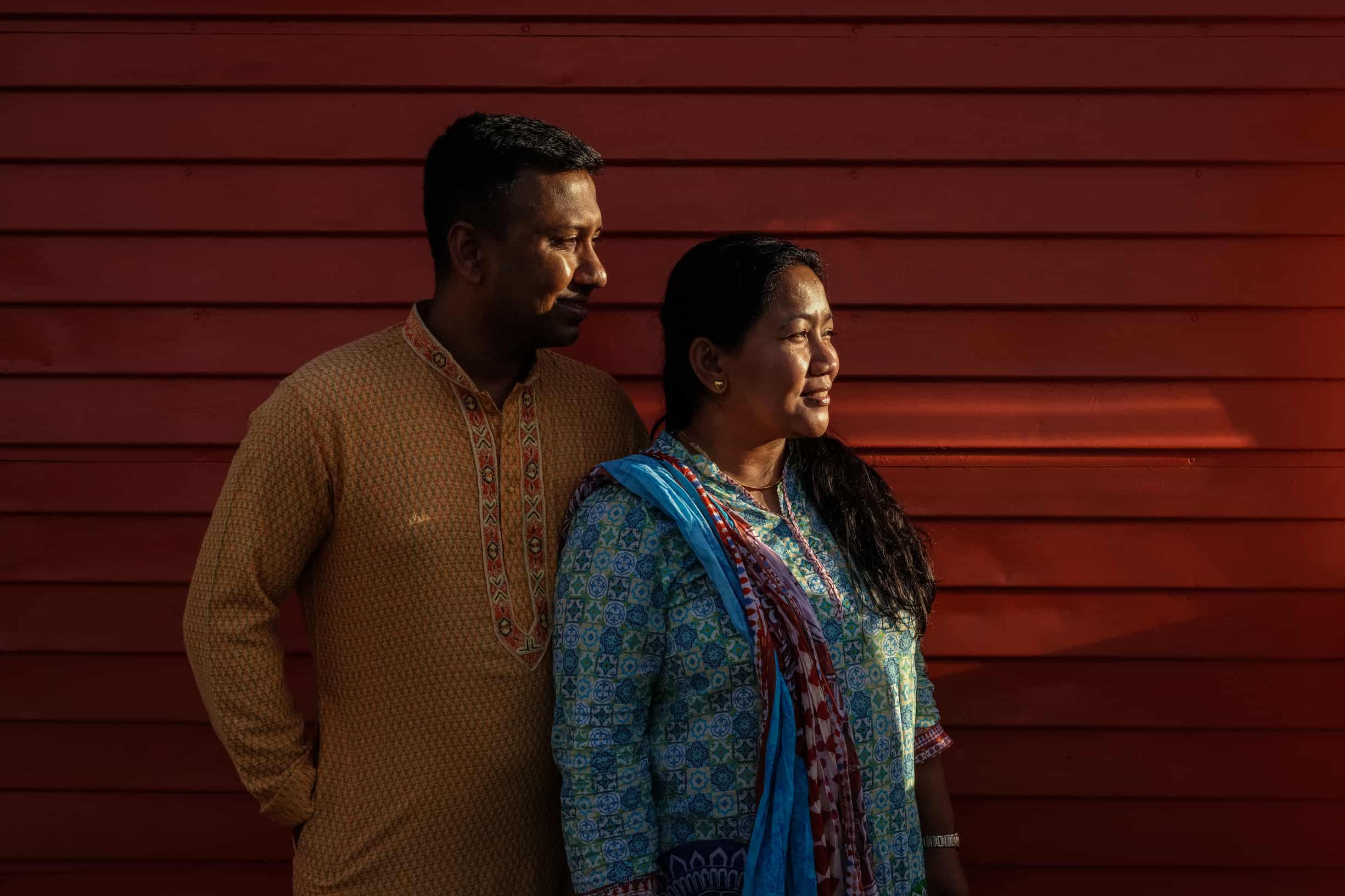 Bangladeshi Americans Mohammed Chishti-Shipu, in panjabi, and his wife Cherry, in salwar kameez, beside the red wood paneled wall of their new home.