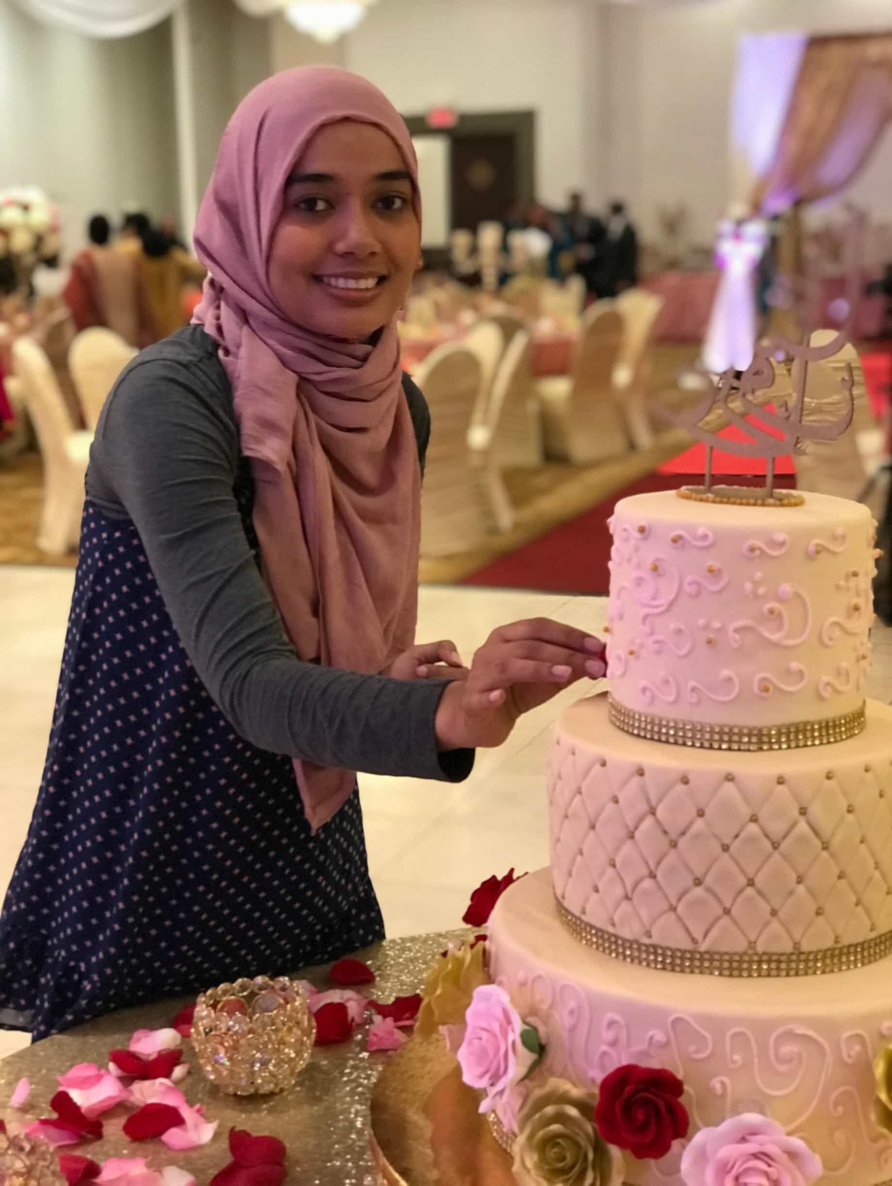 Bangladeshi American Shamsun Nehar wearing a pink hijab with a polka dot dress puts the finishing touches on the three tiered wedding cake she made.