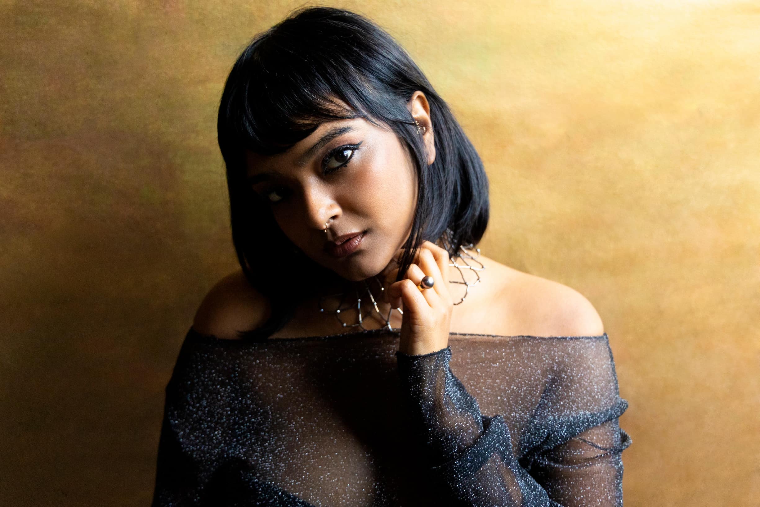 Headshot of Bangladeshi American author and perfumer Tanaïs dressed in a sparkly blue sheer off-the-shoulder top and metal choker necklace.