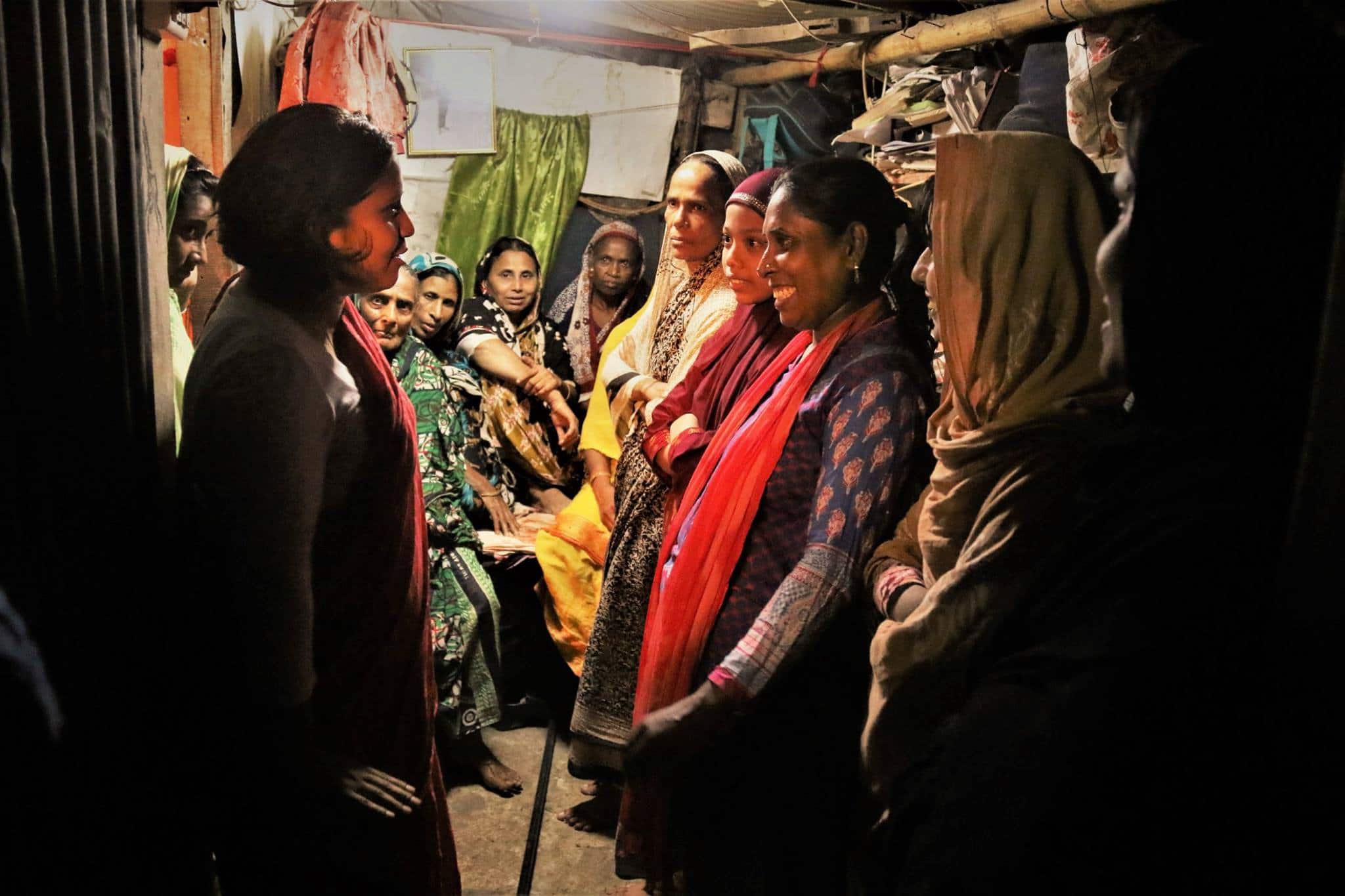 Bangladeshi Chaumtoli Huq on the left speaks with ten female garment workers and organizers who are wearing salwar kameez inside small storage room.