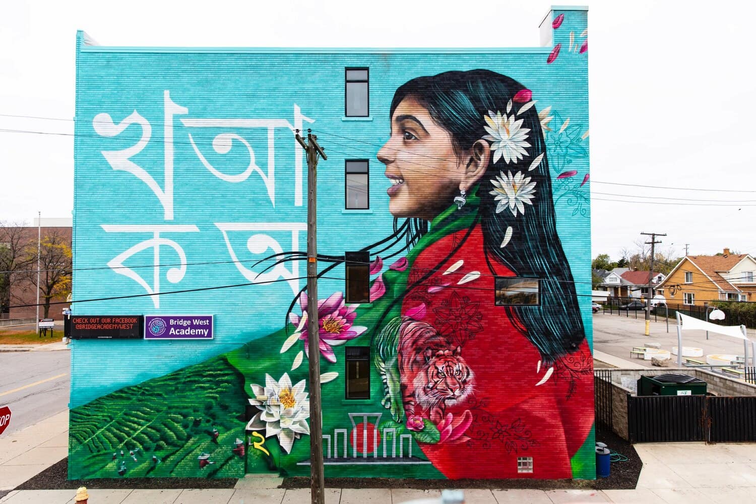 Mural on the side of Bridge West Academy depicts a girl dressed in the Bangladeshi flag with a Bengal tiger, Bengali script, Shaheed Minar and hills.