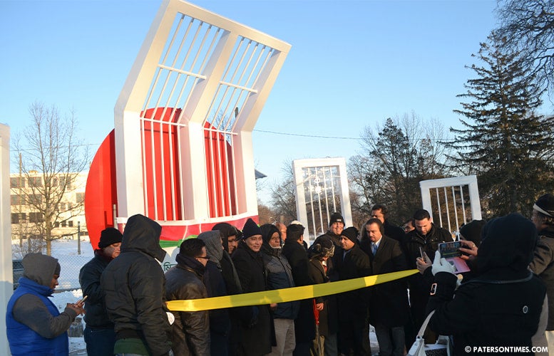 Bangladeshi Americans gather outside on a snowy day behind a yellow ribbon in anticipation of the ceremonial unveiling of the Shaheed Minar replica.