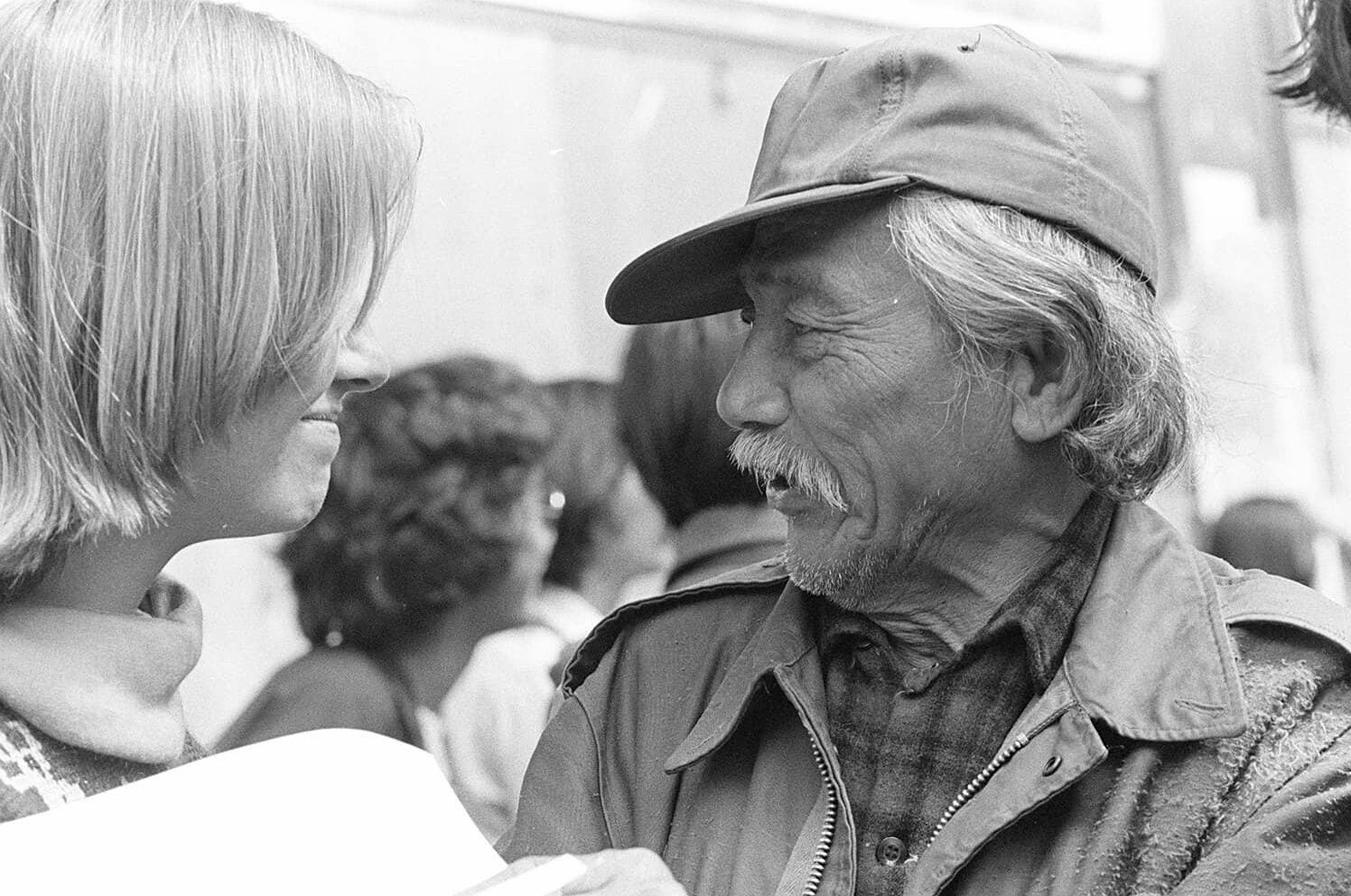 I-Hotel tenant Felix Ayson, dressed in a plaid shirt and collared jacket and wearing a baseball cap, speaks with a supporter on the street.