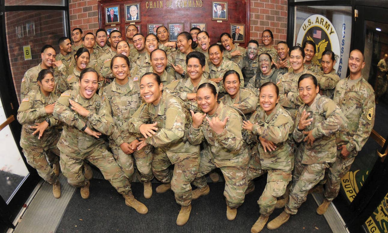 Thirty-five members of a Samoan American family in the U.S. Army, all wearing their uniforms, playfully pose for pictures in a foyer between doorways.