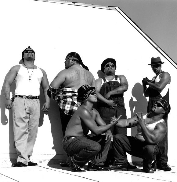 Six men of the Boo-Ya Tribe pose on a rooftop. Two members kneel in front while four members stand behind.