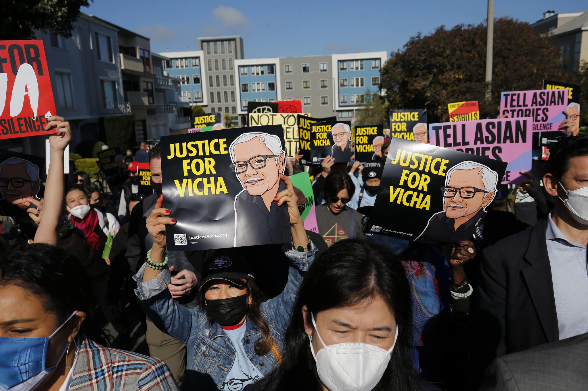 Crowd of people, most of whom wear face masks, gathers outside with signs reading "Justice for Vicha" alongside digital portrait of Ratanapakdee.