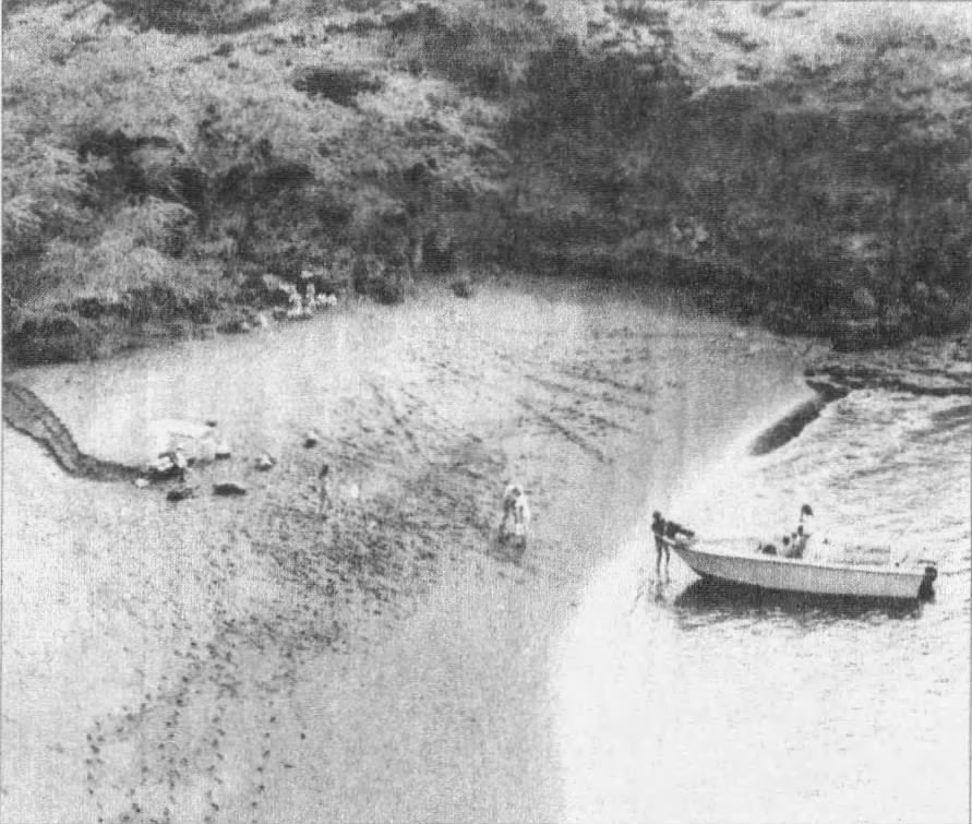 On the shore of Kūheʻeia Bay, a boat sits in shallow water as protestors set up their occupation. Footprints trail across the sand.