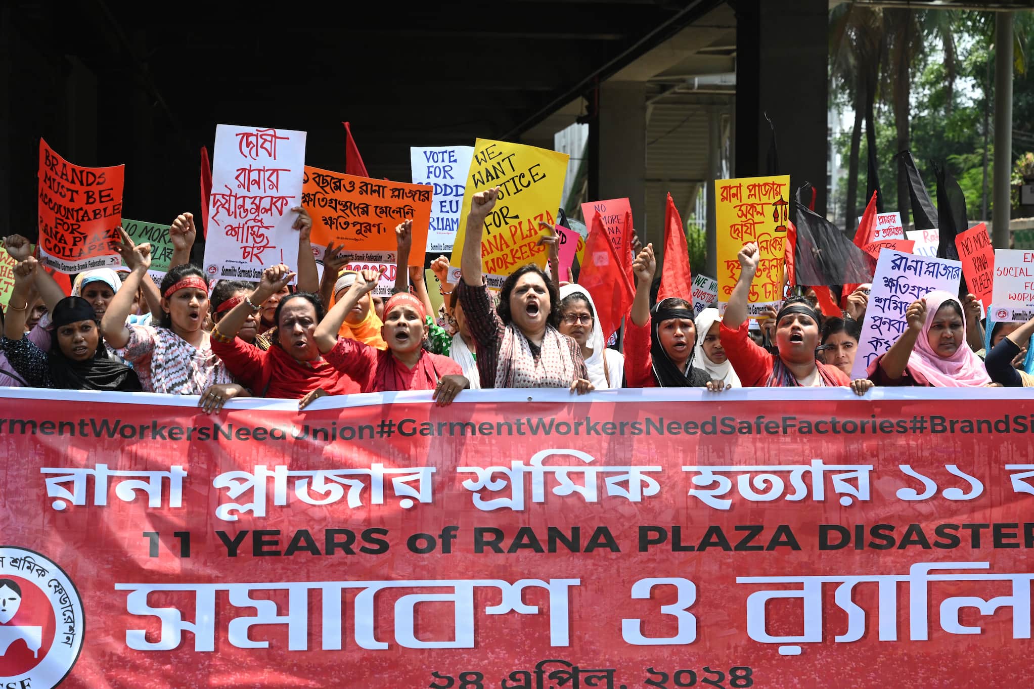 Workers with raised fists gather behind banner marking the anniversary of the Rana Plaza building collapse.