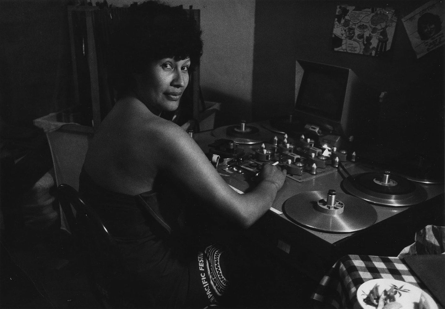 Māori filmmaker Merata Mita, wearing a strapless dress, sits before a flatbed editing machine.