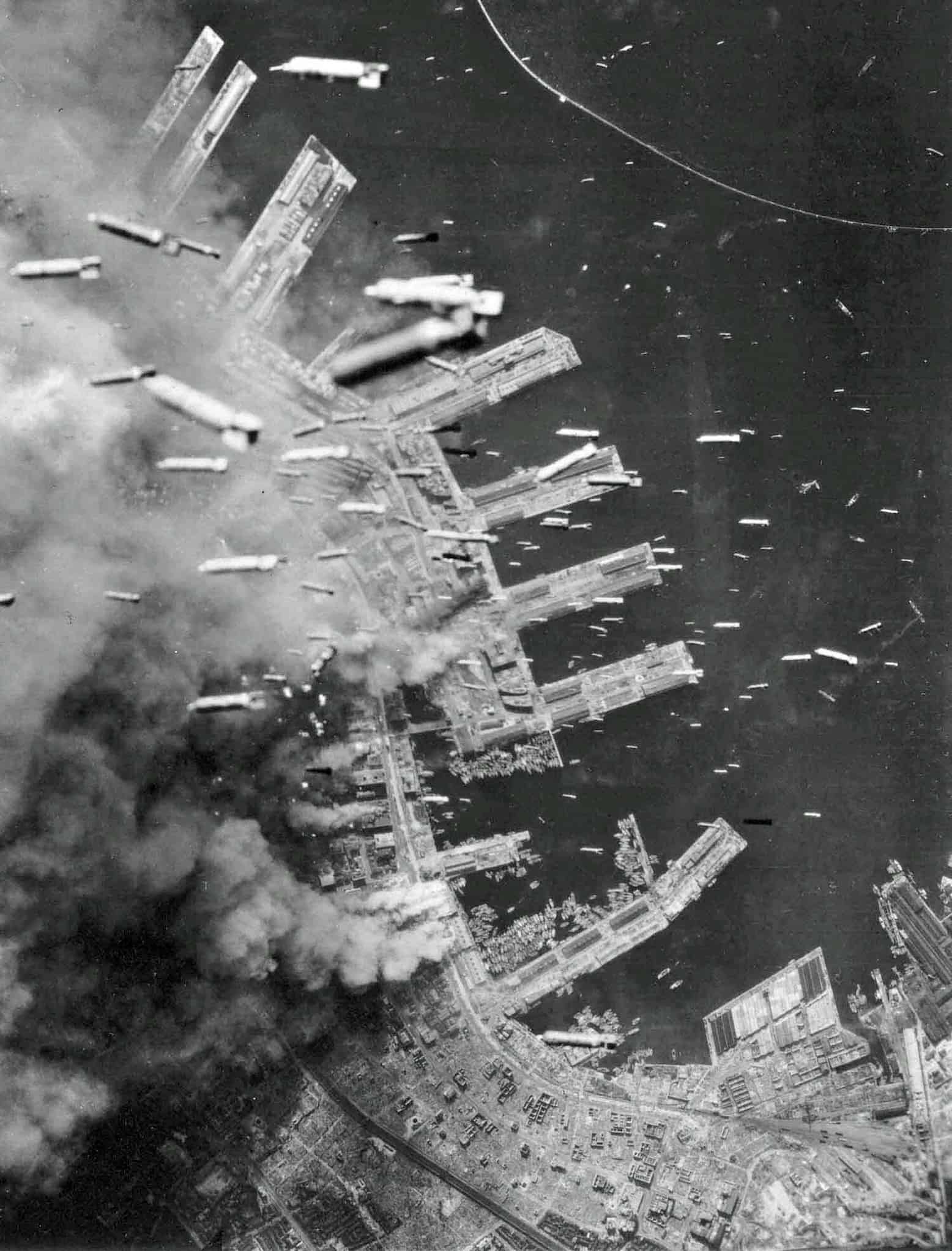 Aerial view from B-29 American bombers as they drop incendiary bombs onto the burning port city of Kobe. Clouds of smoke billow from the fires.