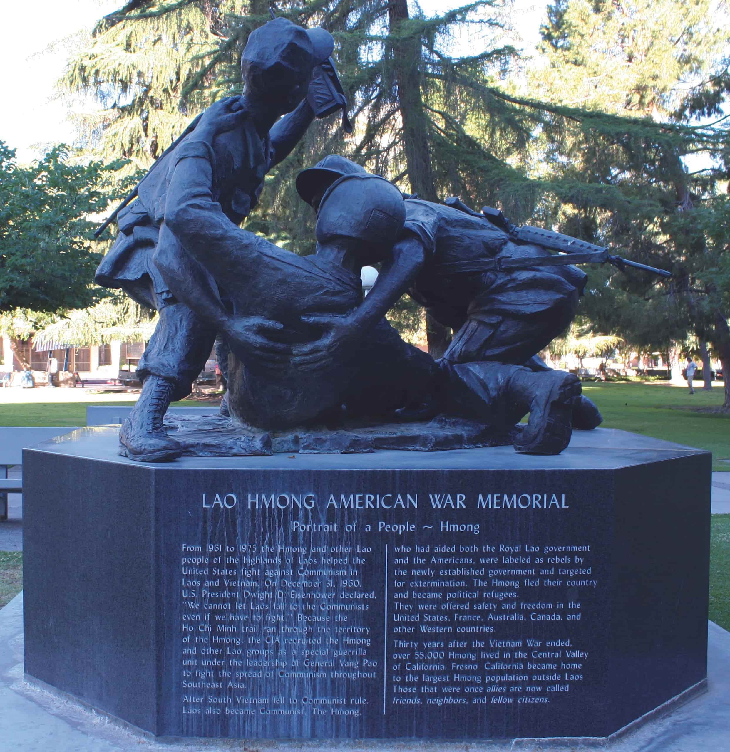 The bronze statue shows two soldiers crouched to help a fallen soldier. "Lao Hmong American War Memorial" is written at the base of statue.