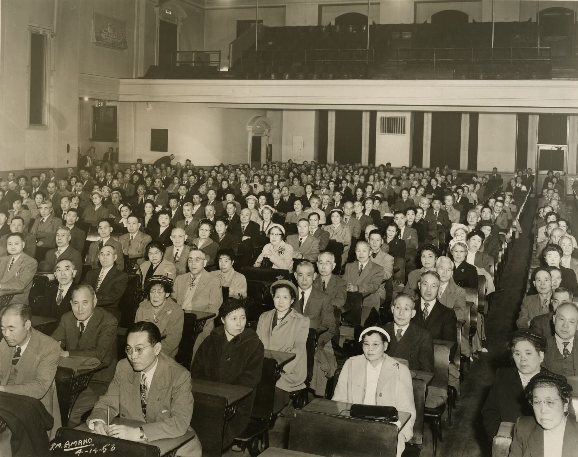 An audience of elderly Japanese Americans sit in auditorium for a mass naturalization ceremony.