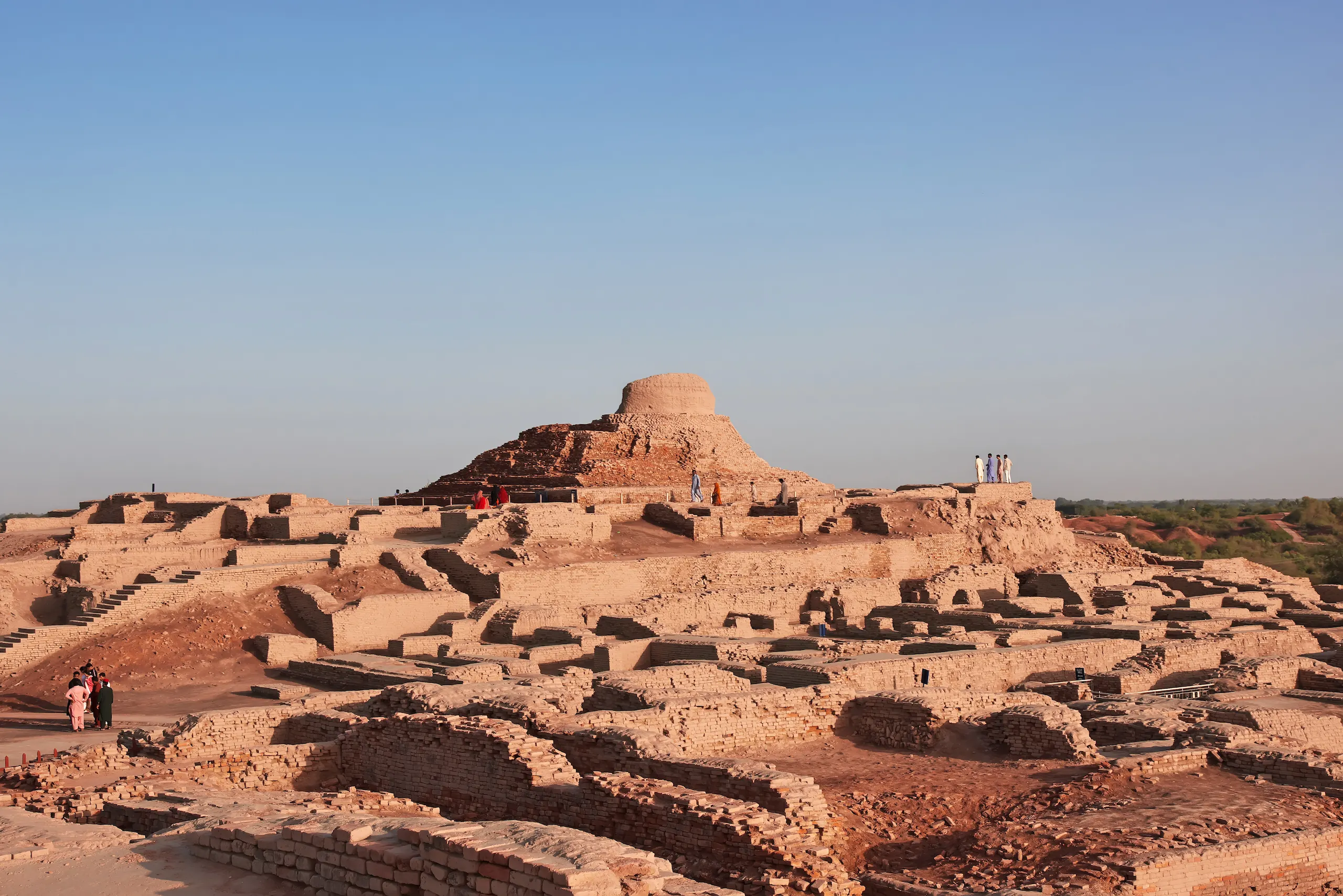 Wide view of ancient city's remains across desert landscape. Crumbling brick walls and stairs are arranged in grid-like pattern.
