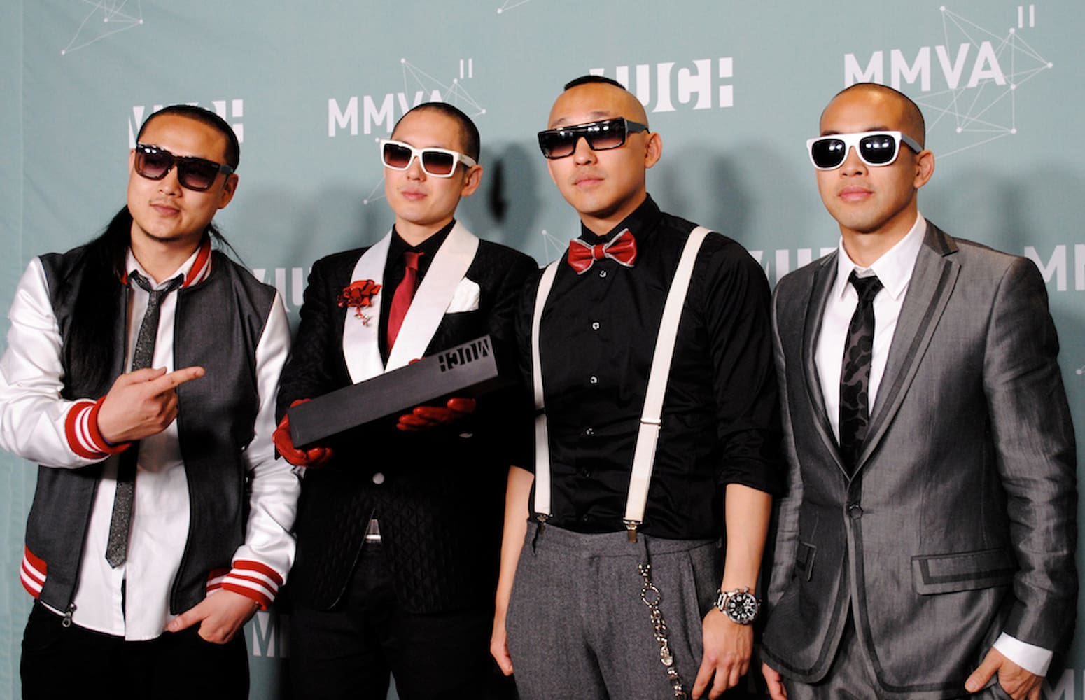 Four members of Far East Movement, an all-Asian American hip hop group, pose at awards show. The four men wear formal attire and sunglasses.