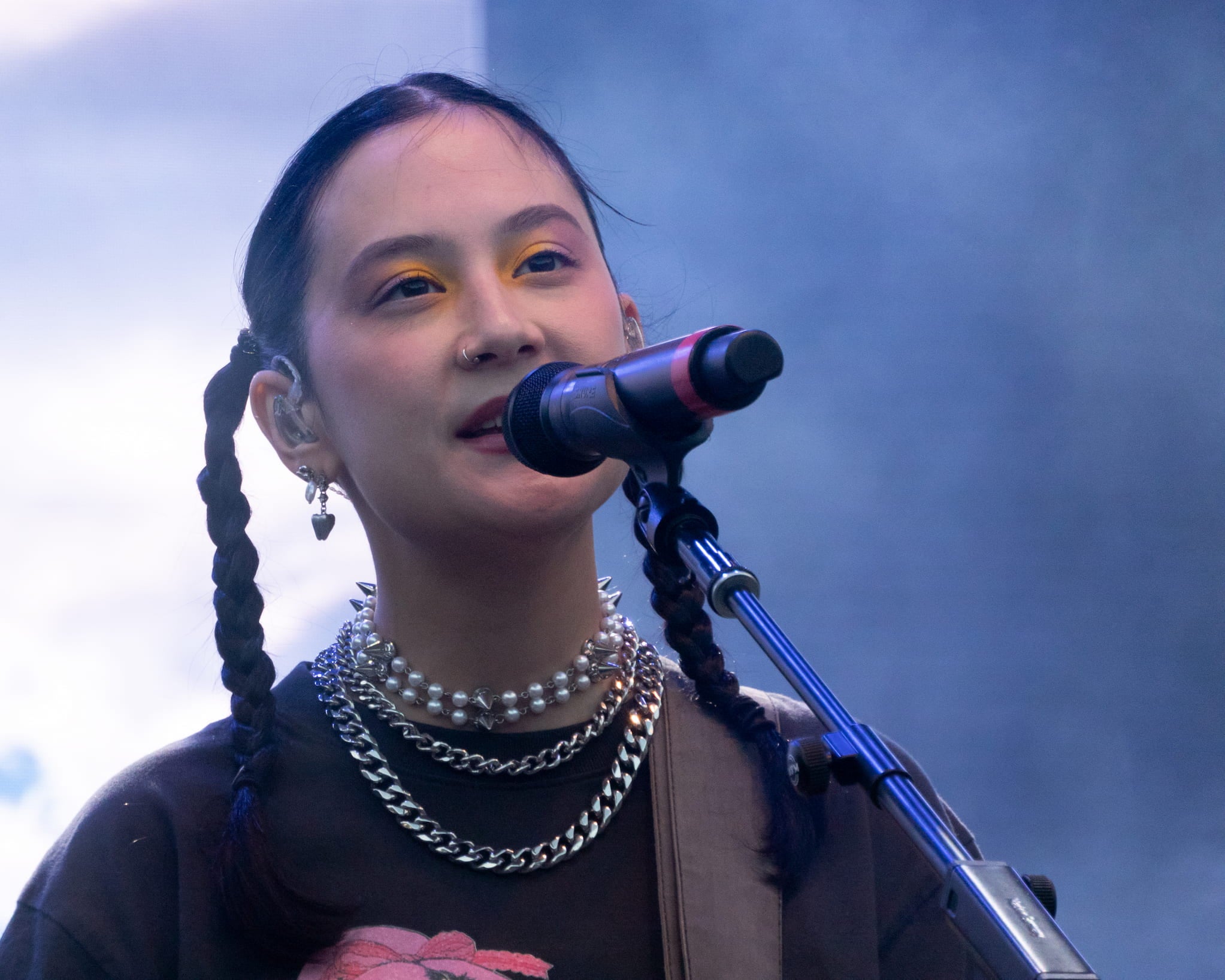 Michelle Zauner, a Korean American woman with dark hair braided into twin braids and wearing three necklaces, sings into microphone on stage.