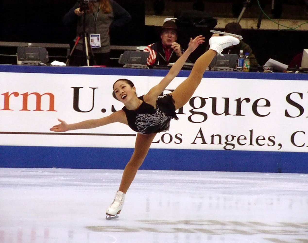 Michelle Kwan, dressed in an embroidered figure skating dress, performs a spiral move, gliding on ice with one leg extended straight behind her.