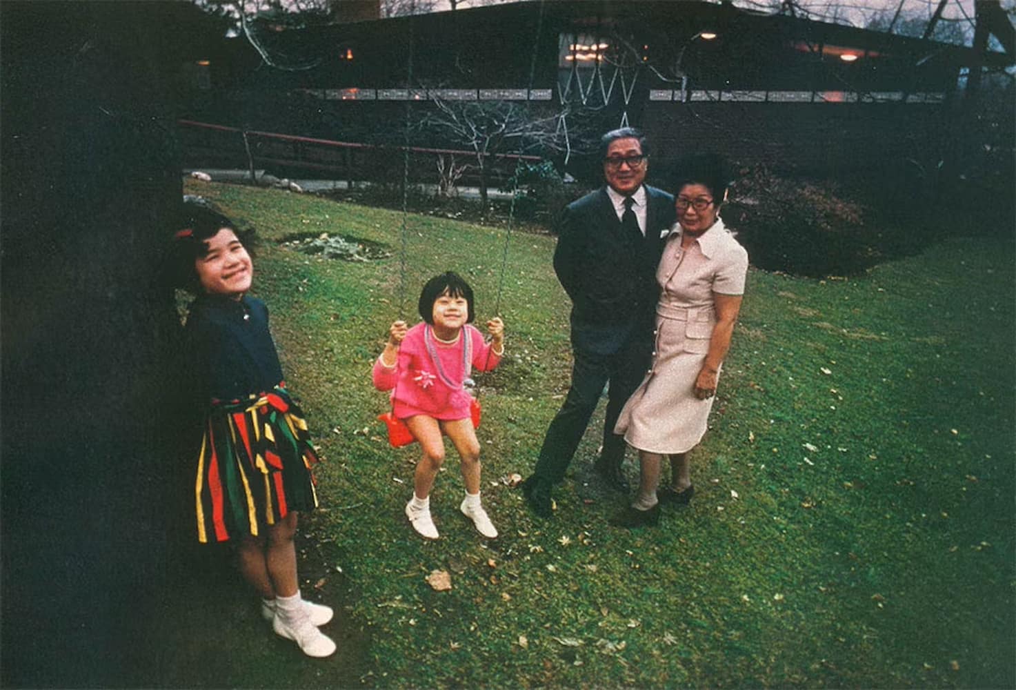 Japanese American Keiichi Sugahara, dressed in a suit, poses with his wife in a shirt dress and his smiling granddaughters on the lawn of his manor.