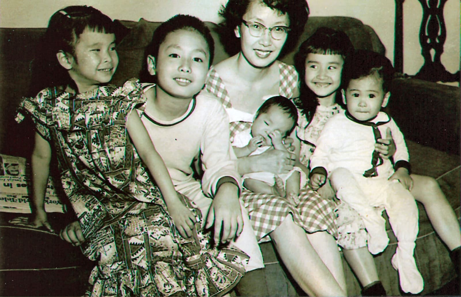 Japanese American Yuri Kochiyama, wearing a plaid dress, holds her baby in her lap while sitting between her four children on the couch.