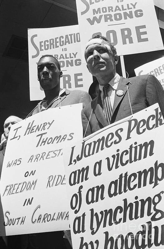 White American activist James Peck, with bandages on his head, and Henry Thomas, an African American man, hold signs as they stand in picket line.