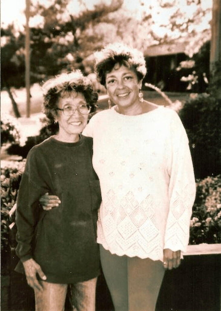 Yuri Kochiyama, in a sweater and jeans, stands with her arm around Puerto Rican Dylcia Pagan, dressed in crocheted sweater and leggings.