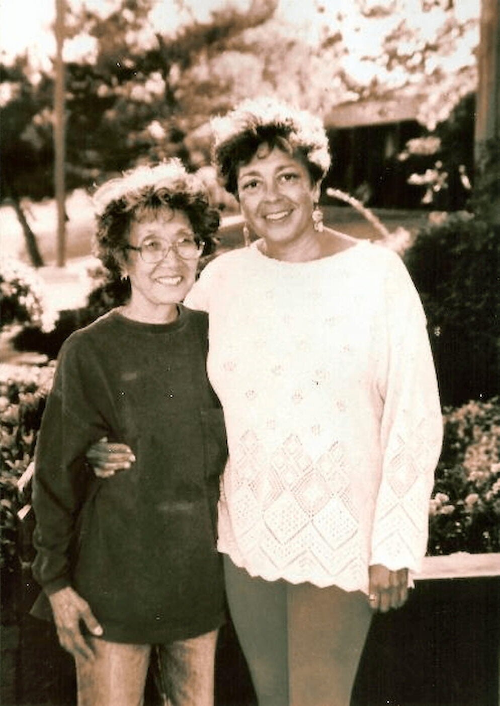 Yuri Kochiyama, in a sweater and jeans, stands with her arm around Puerto Rican Dylcia Pagan, dressed in crocheted sweater and leggings.