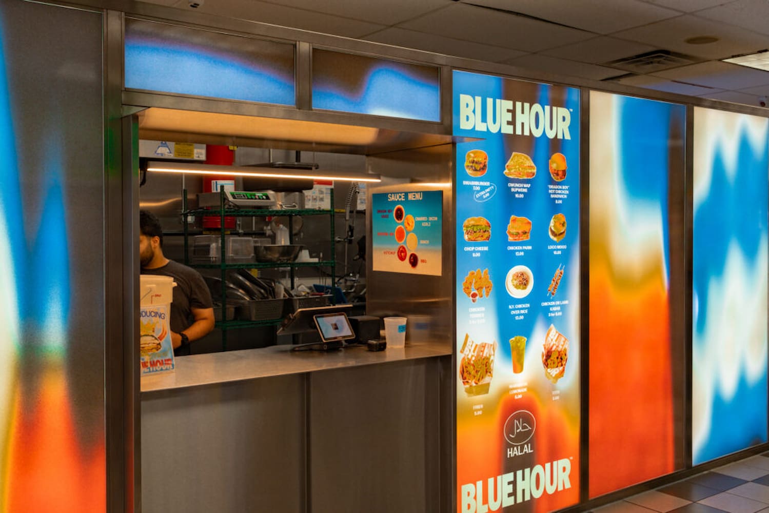 Order counter and kitchen at Blue Hour. On either side of counter are backlit multi-colored panels, with the menu displayed as images to the right.