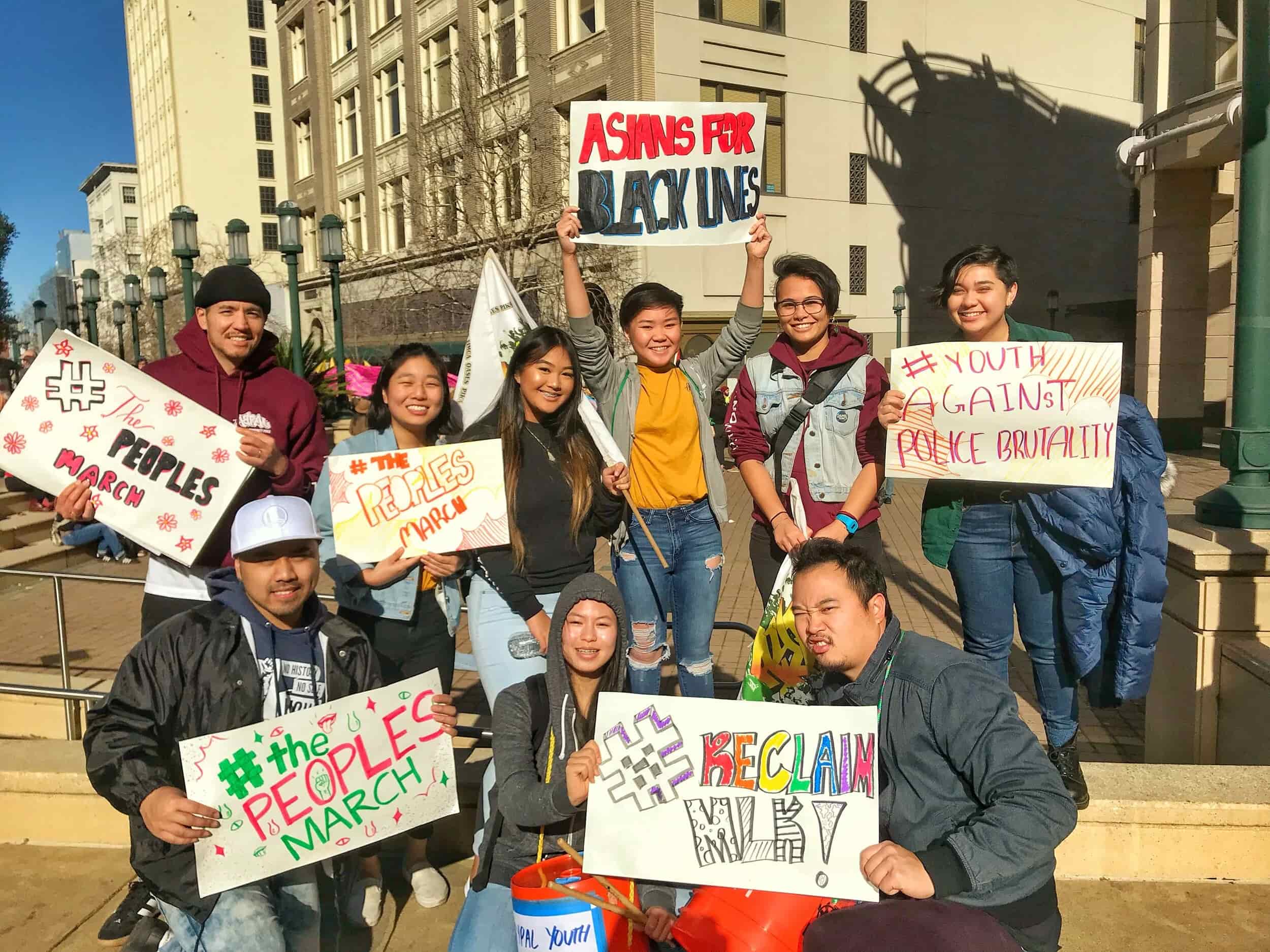 Nine AYPAL members, gathered outside building, pose with signs that show support for the Black Lives Matter movement.