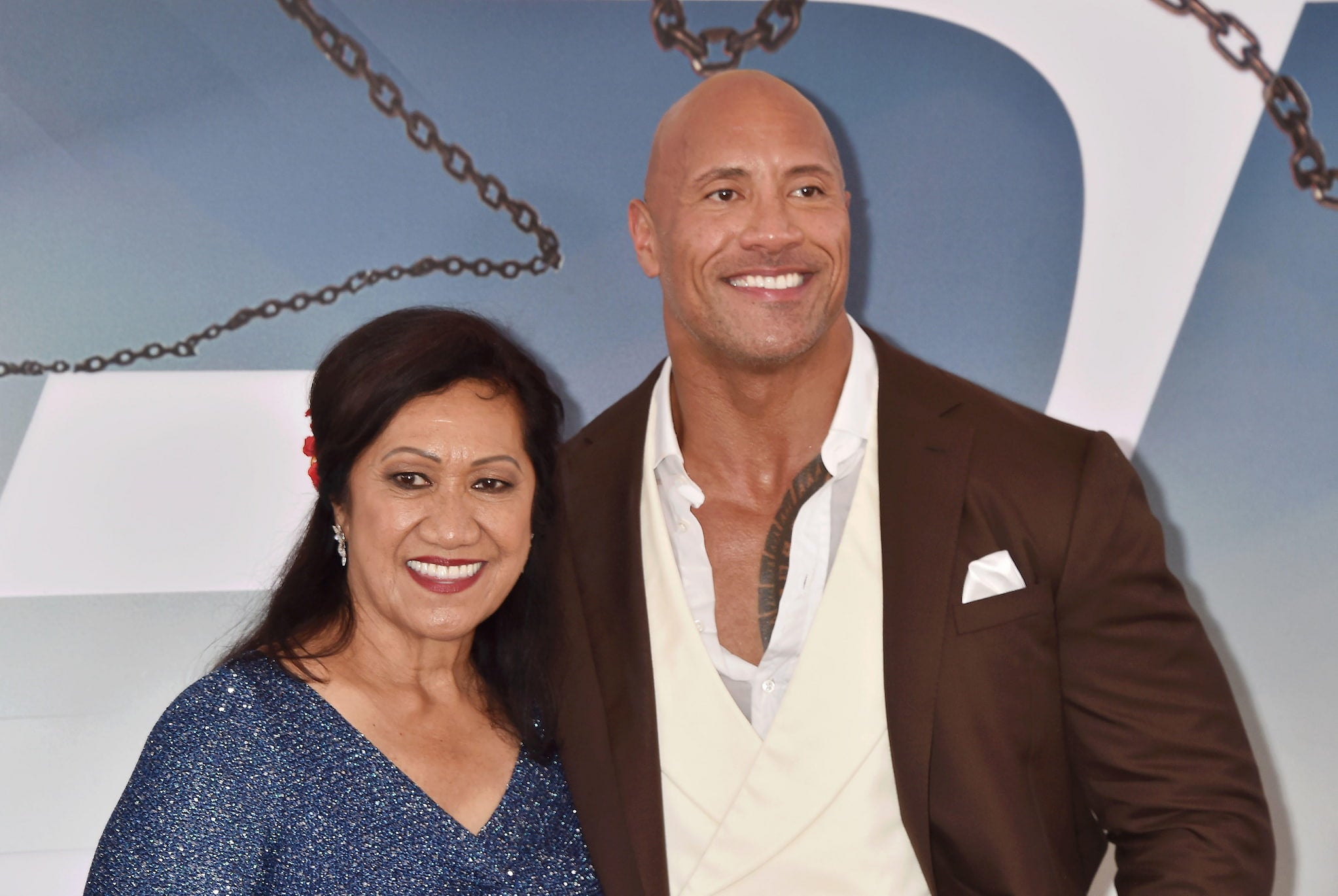 Actor Dwayne Johnson, dressed in a suit, vest and unbuttoned collared shirt, poses with Ata Johnson, dressed in a sparkly long sleeved dress.