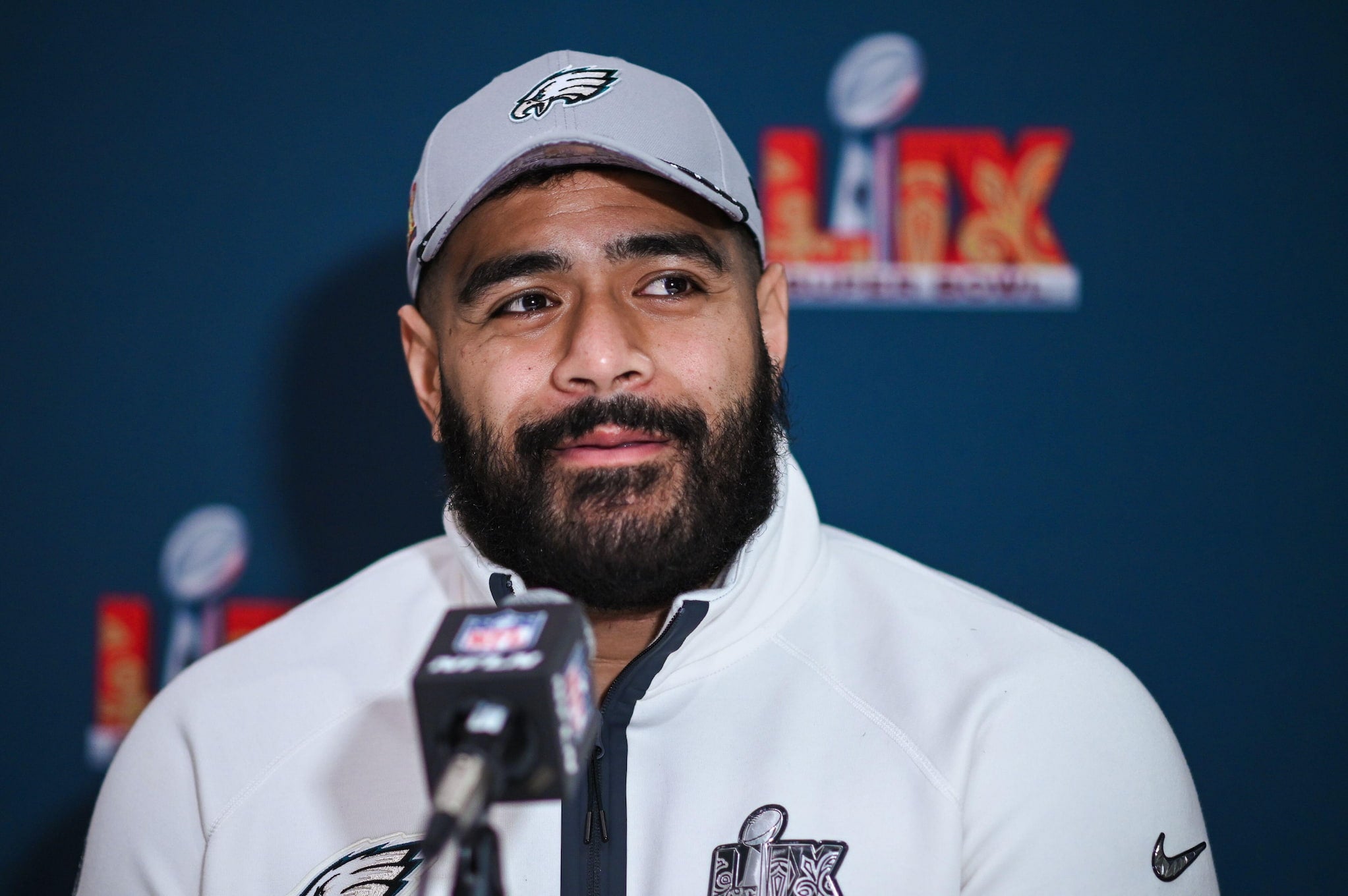 Australian footballer Jordan Mailata, dressed in an Eagles jacket and cap, sits in front of a NFL microphone for a media conference.