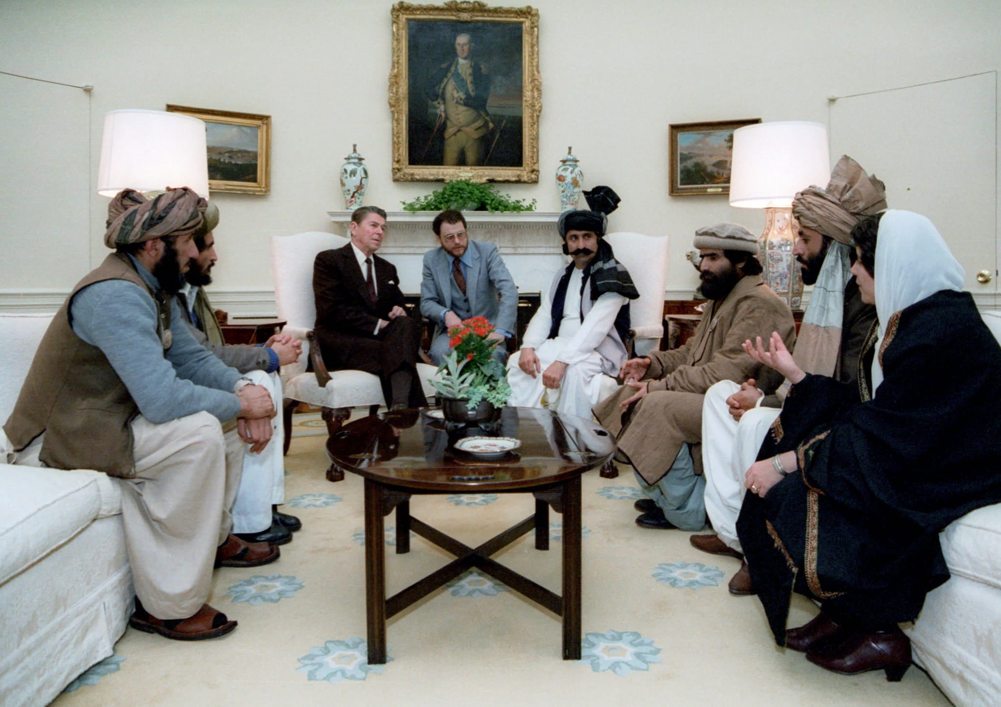 President Ronald Reagan, at center, meets with six leaders of mujahideen, who sit across from each other on two couches.