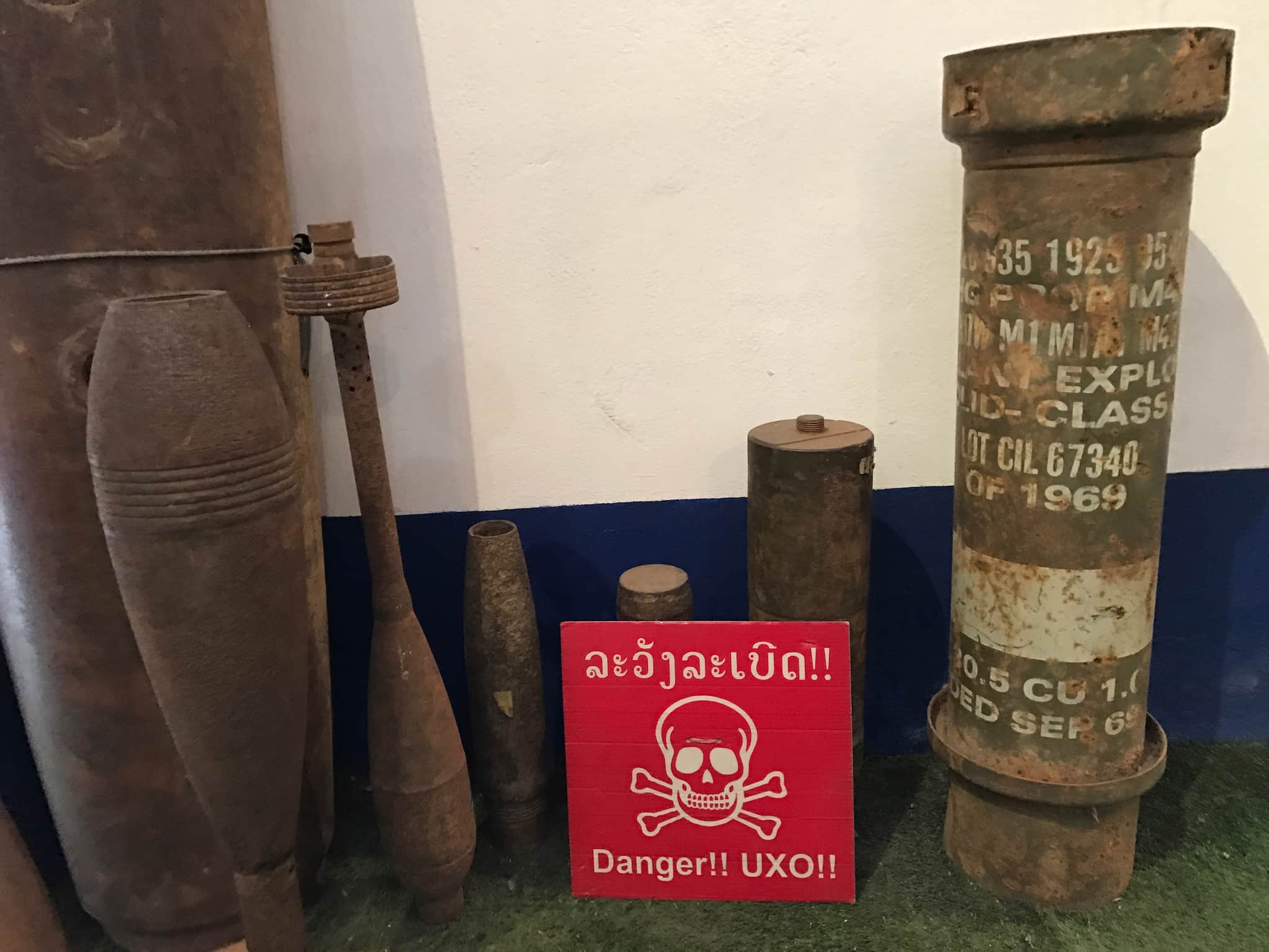 Museum display shows bombs dropped in Laos by the U.S. A sign in Lao and English reading "Danger!! UXO!!" appears in front of display.