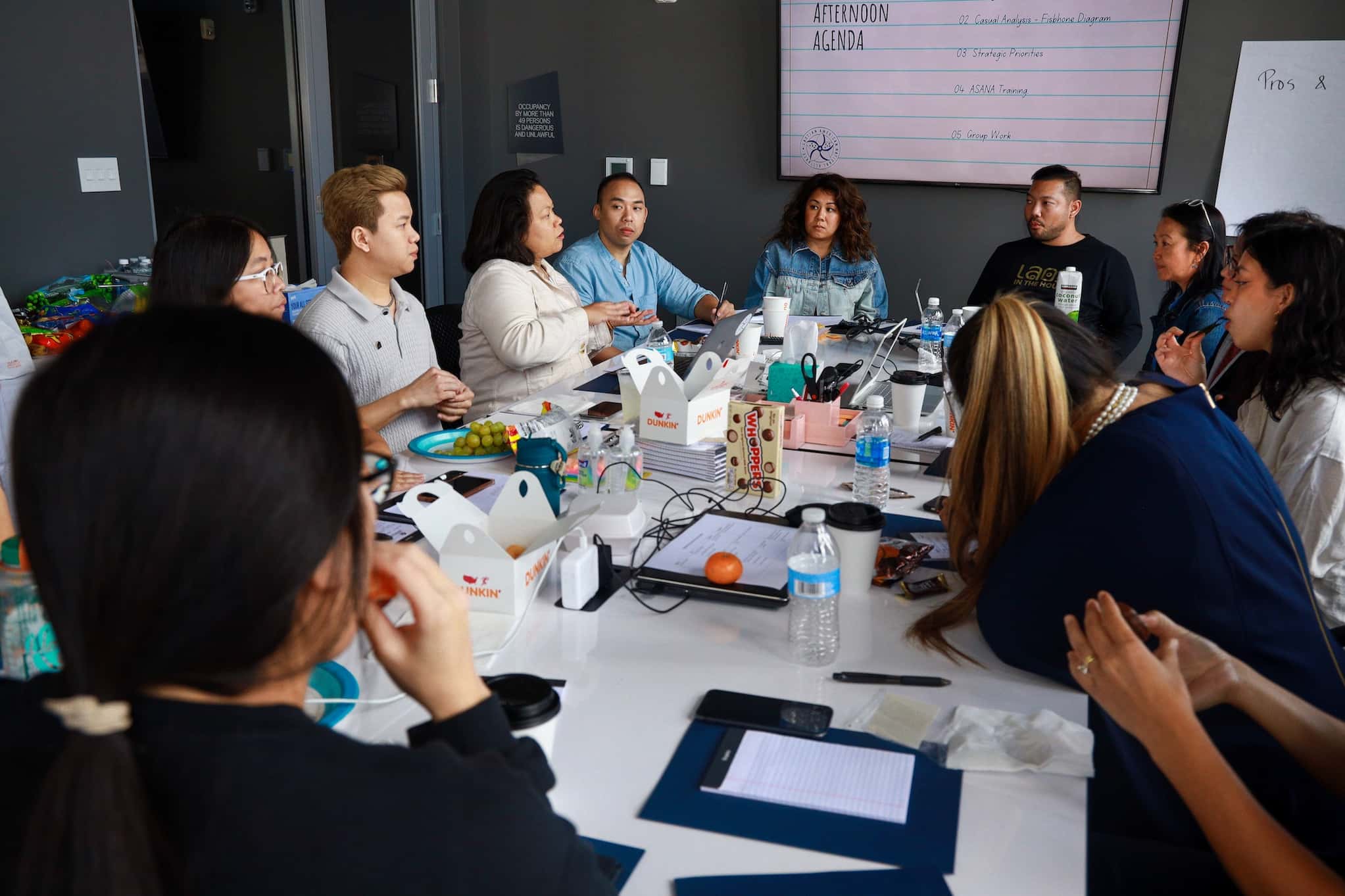 Twelve members of the Laotian American National Alliance attend a meeting around a conference table. Snacks and office supplies cover the table.