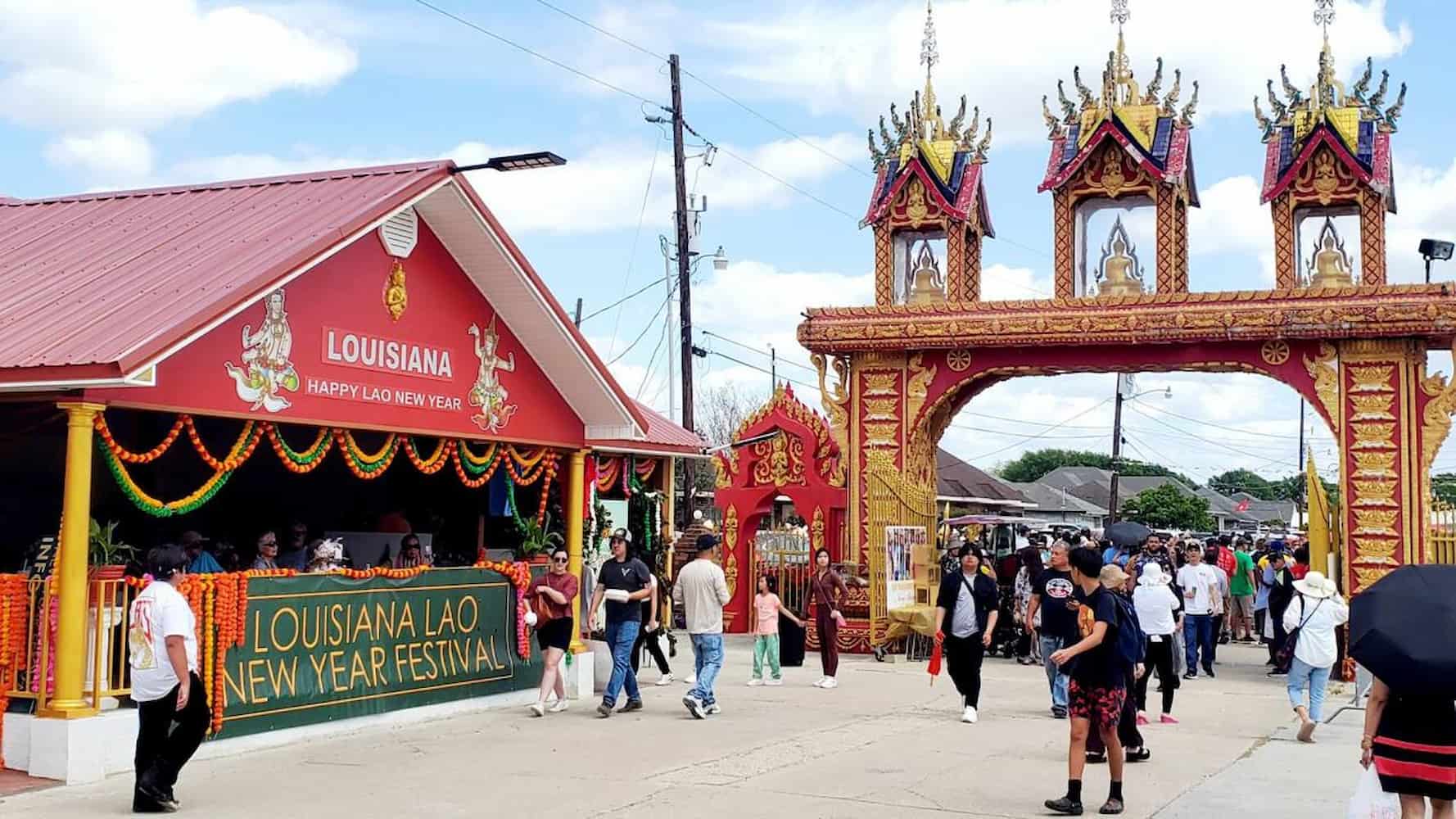 A large crowd waits to enter through arched temple gate. A covered pavilion has a banner that reads "Louisiana Lao New Year Festival."