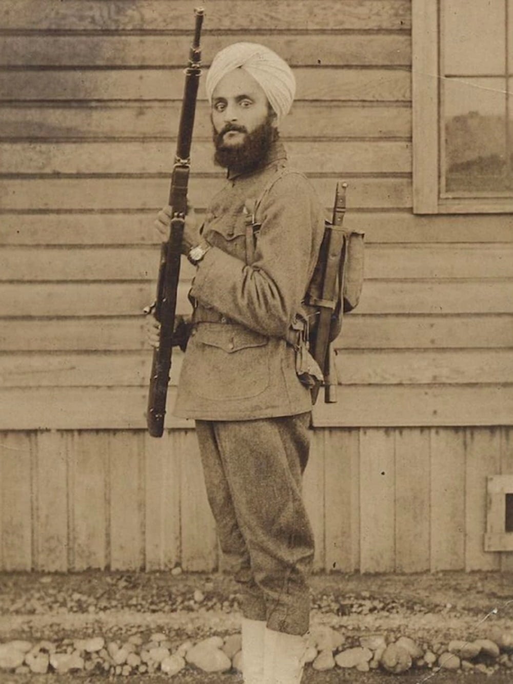 Bhagat Singh Thind, a Sikh man, in his U.S. military uniform and turban, standing at attention with his rifle and gear.