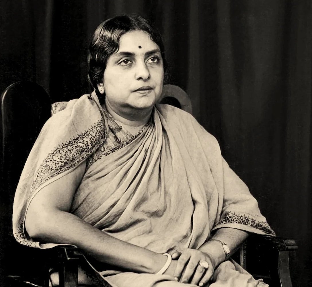 Indian activist Kamaladevi Chattopadhyay, dressed in a saree, sits in an armchair with her hands loosely clasped in her lap.