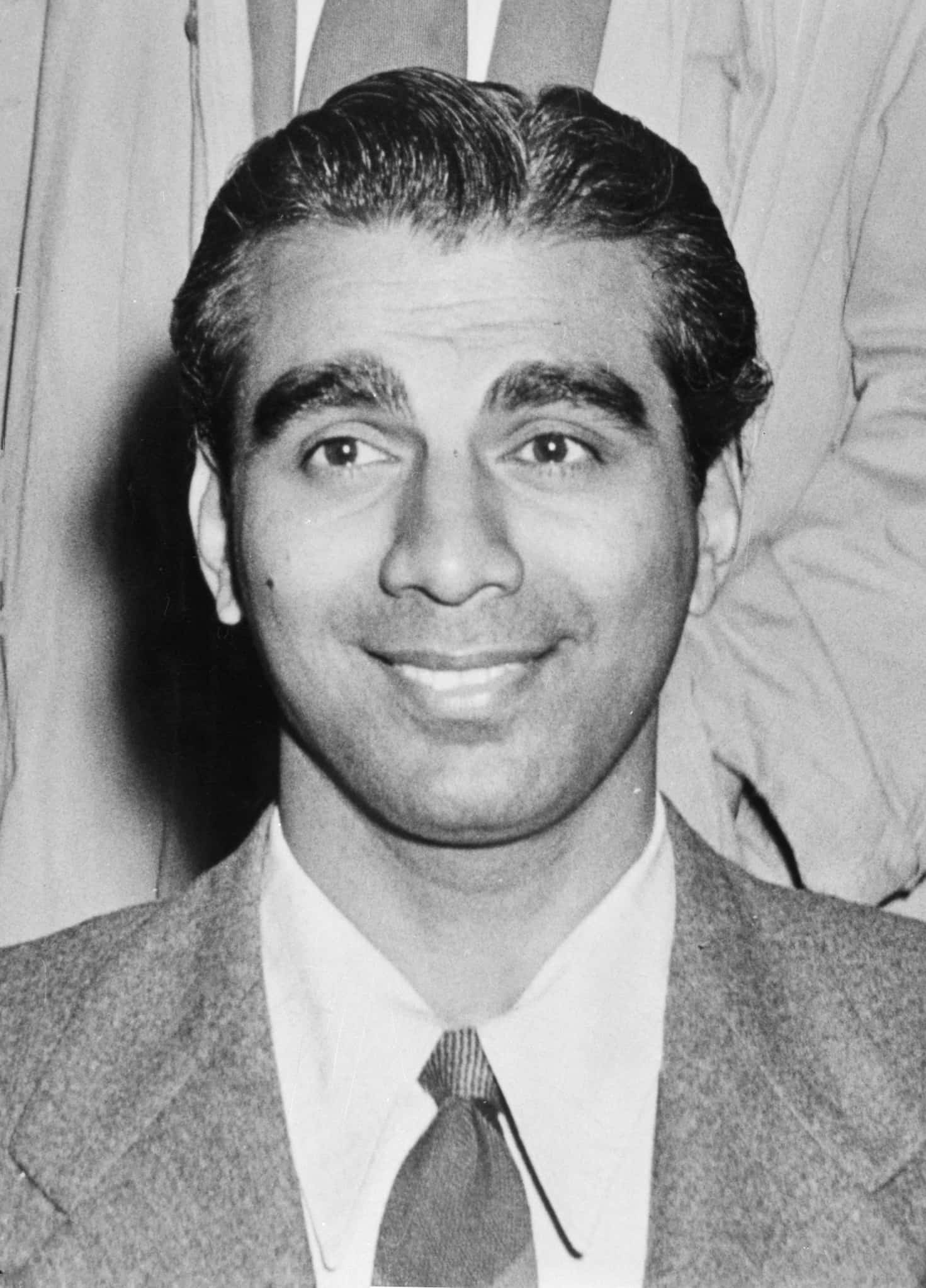 Indian Cheddi Jagan, dressed in a suit and tie, smiles and looks towards someone off-camera in candid photo.