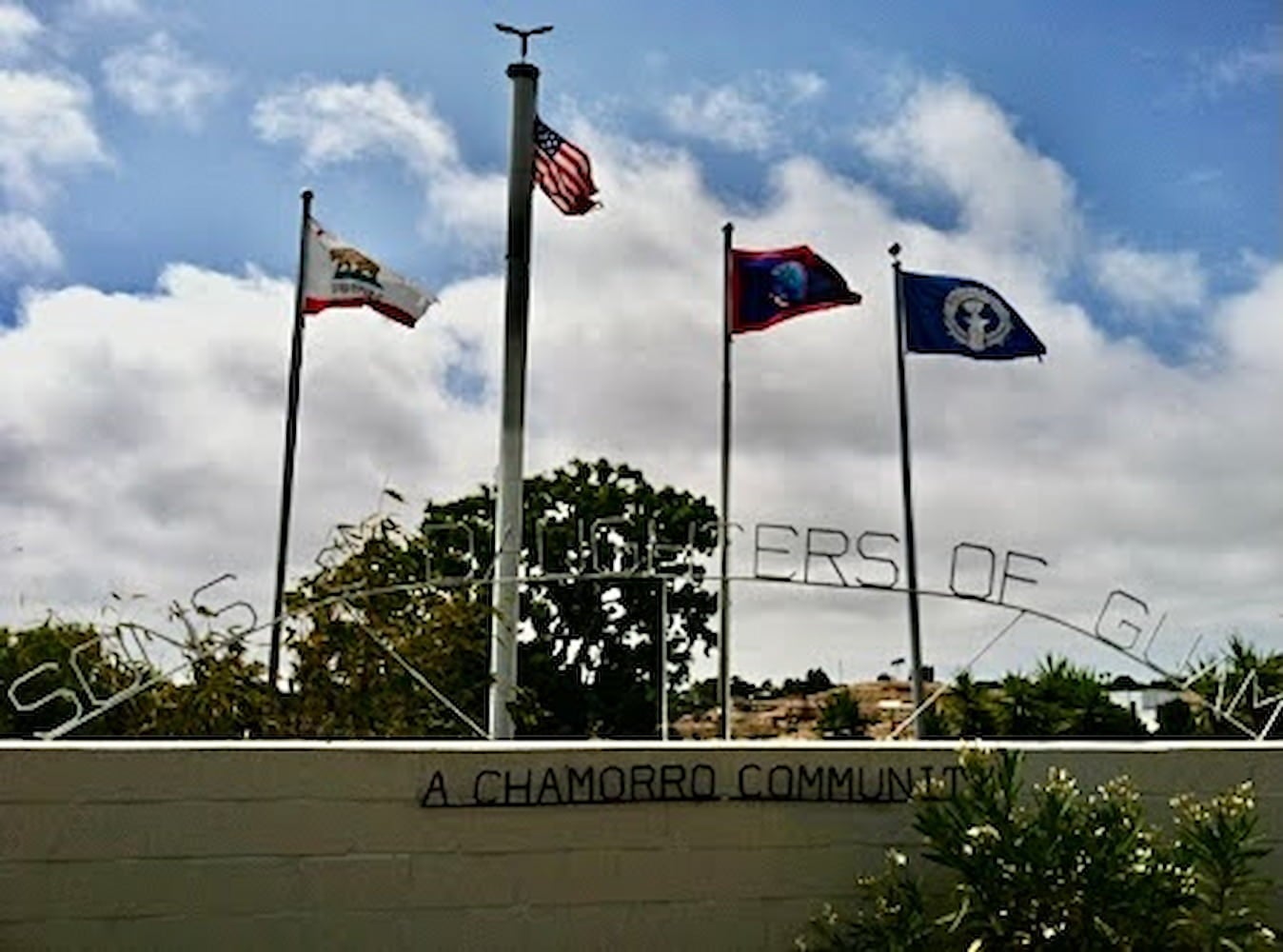 The entrance of the Sons and Daughters of Guam Club with the flags of California, U.S., Guam, and Northern Mariana Islands flying on flagpoles.