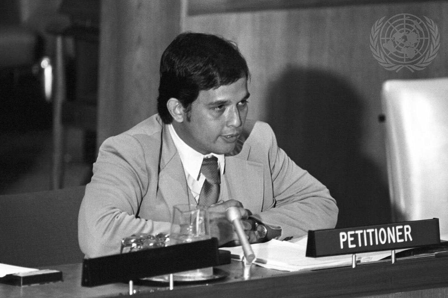 CHamoru Robert Underwood, dressed in a light colored suit, addresses the United Nations while seated behind a "Petitioner" placard.