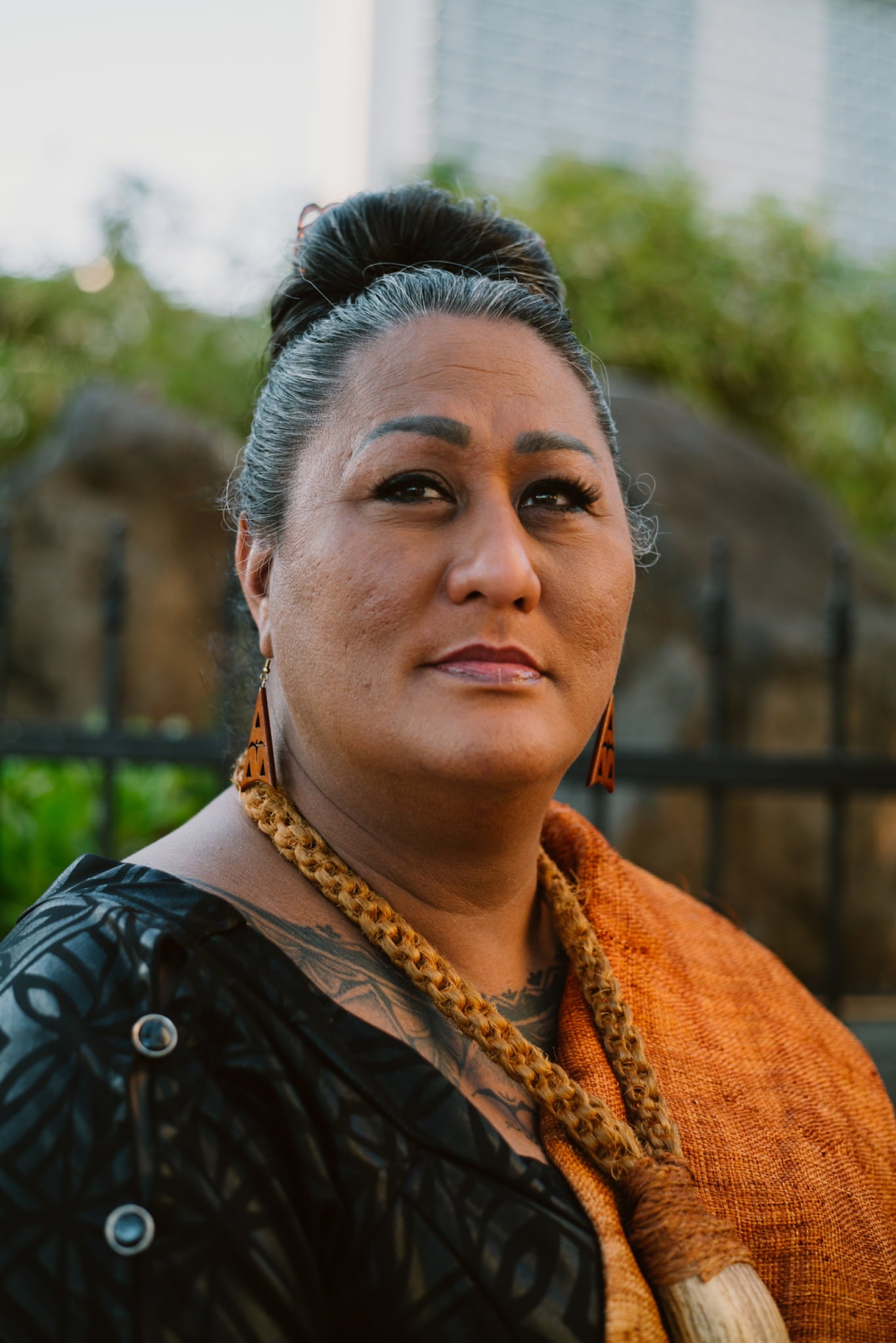 Hina Wong-Kalu, wearing a dress covered by a patterned wrap over her shoulder and a braided lei, poses in outdoor portrait.