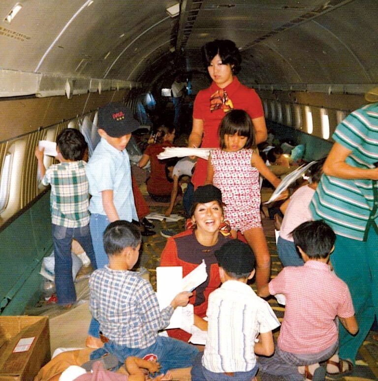 Children play inside of an airplane as flight attendants dressed in red sit, chat, and assist them.