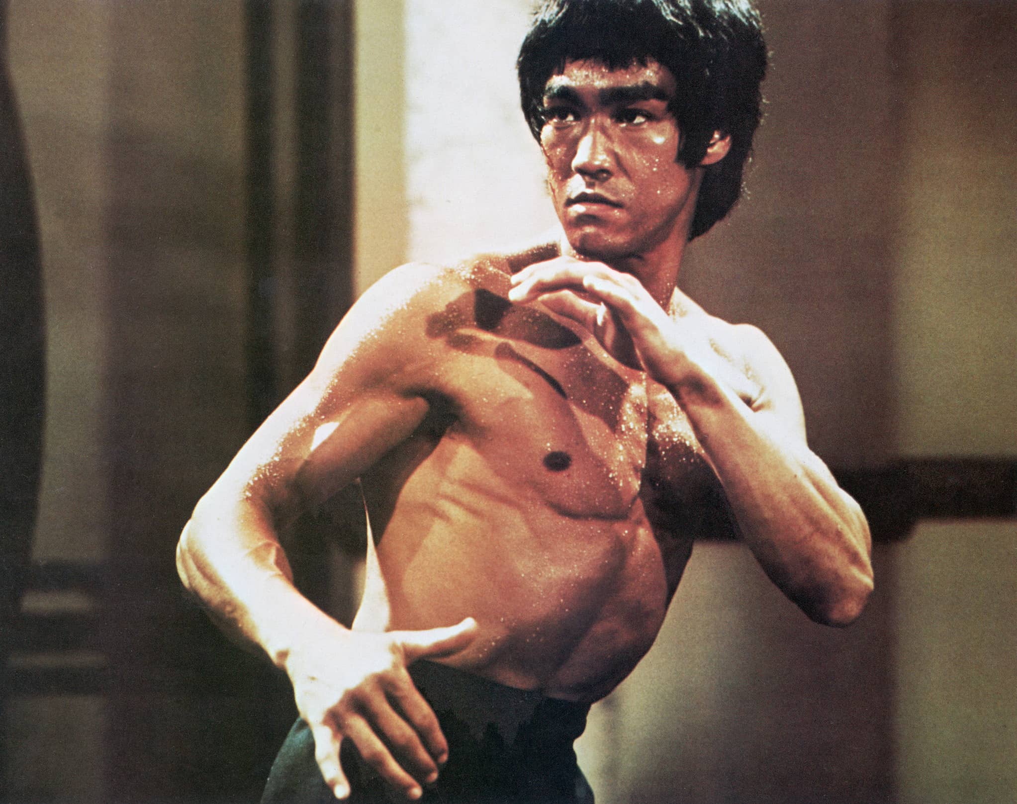 Bruce Lee, a Hong Kong-born American martial artist and actor, poses shirtless in fighting stance with arms raised in front of his chest.