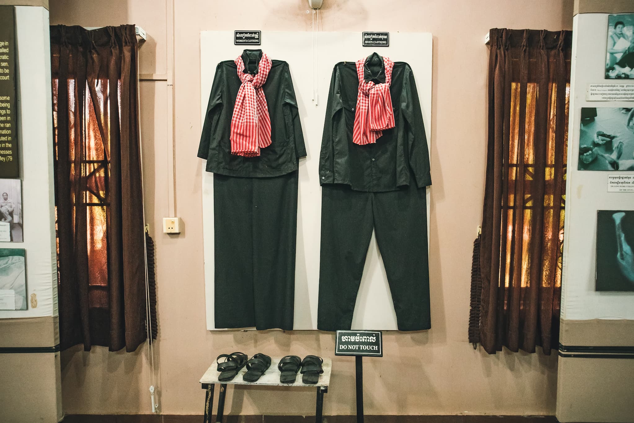 The displayed Khmer Rouge uniforms consist of black long-sleeved shirts and pants with a red checkered woven cloth tied at the neck.