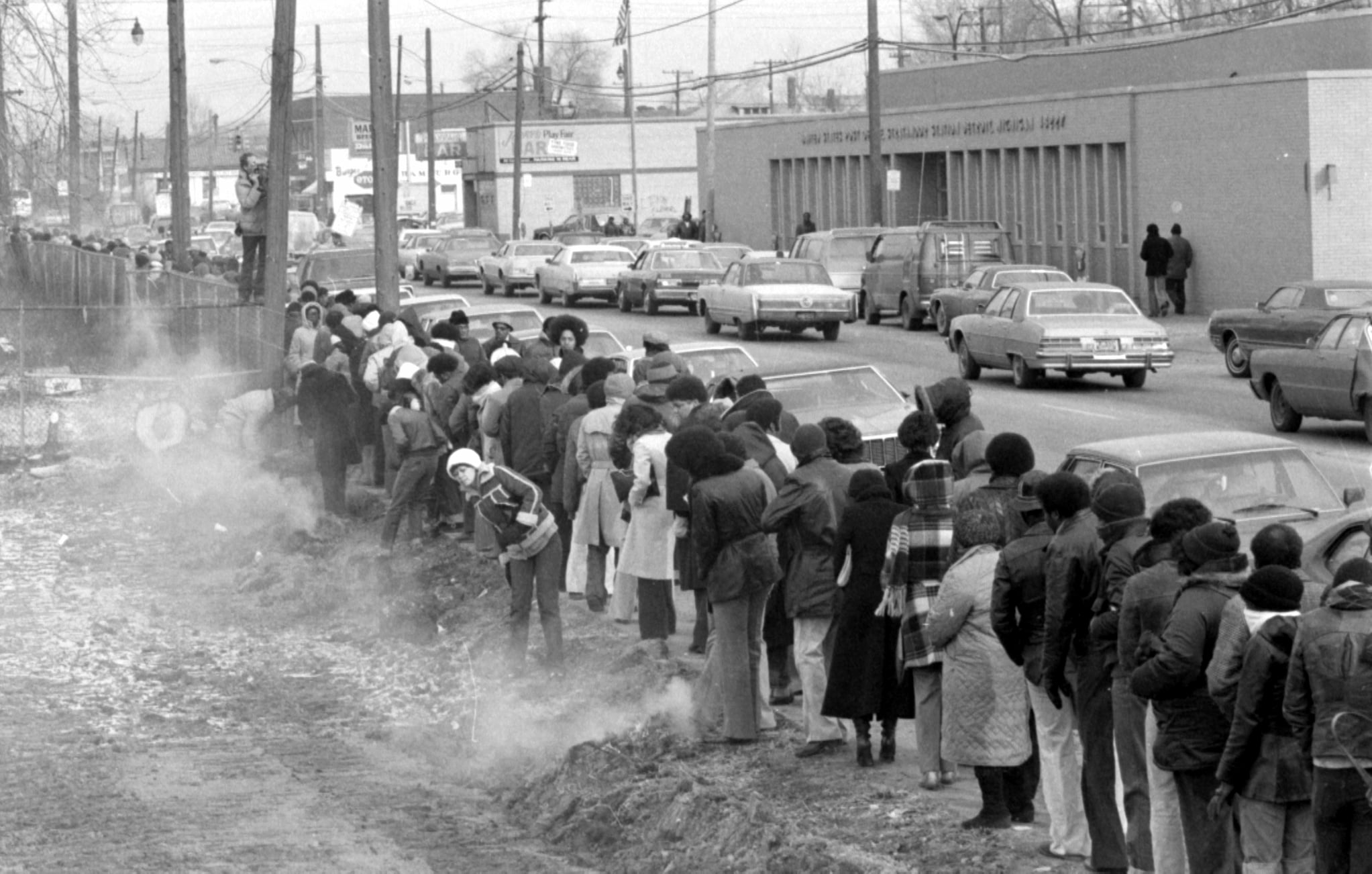 Lines of people, dressed in cold weather clothes, stand in long lines for the Michigan Employment Security Commission that stretch down the sidewalk.