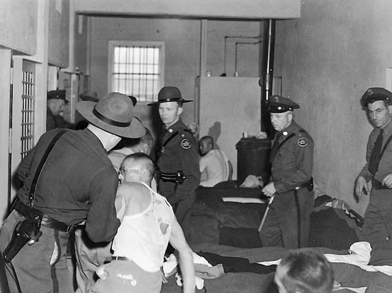 Several officers crowd around an inmate as he is grabbed by the arm in the Tule Lake jail. The inmate's clothes are ripped.