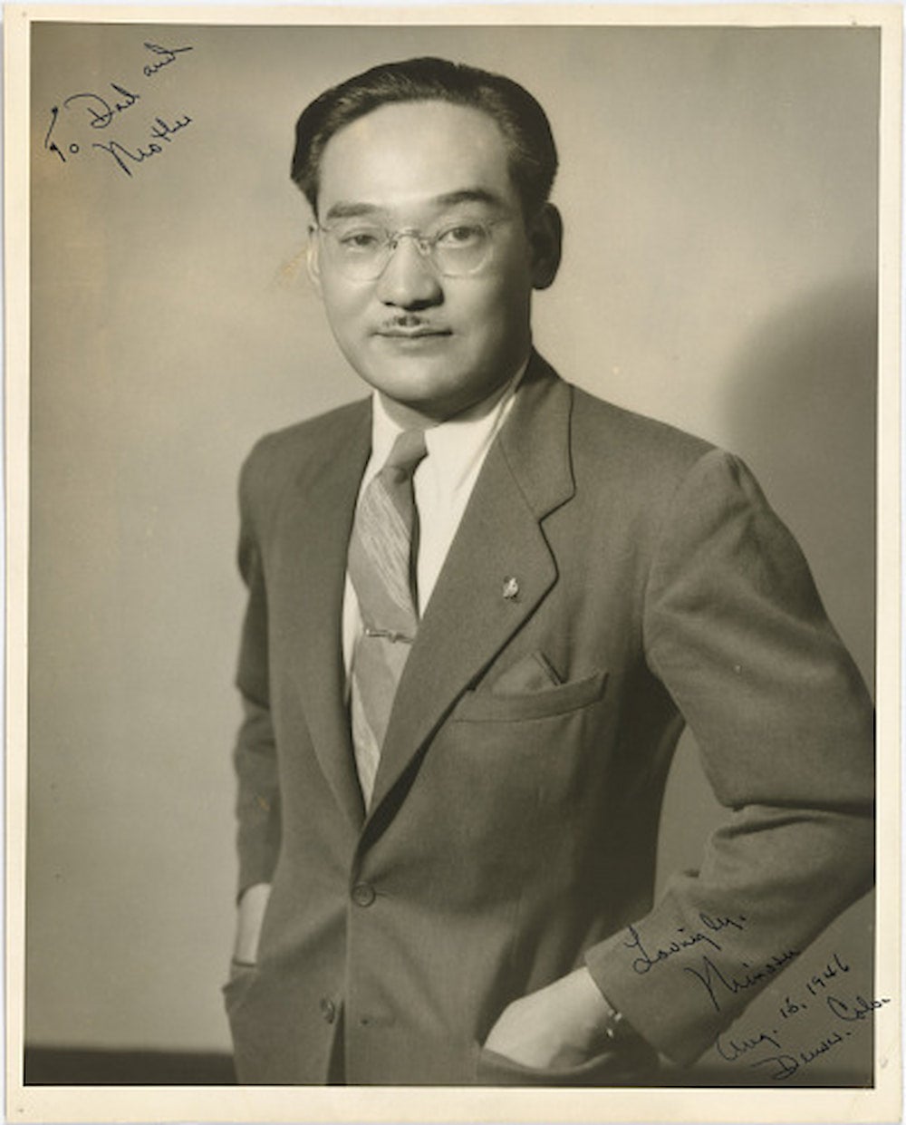 A portrait of Japanese American activist Minoru Yasui in a suit with his hands in his pockets.