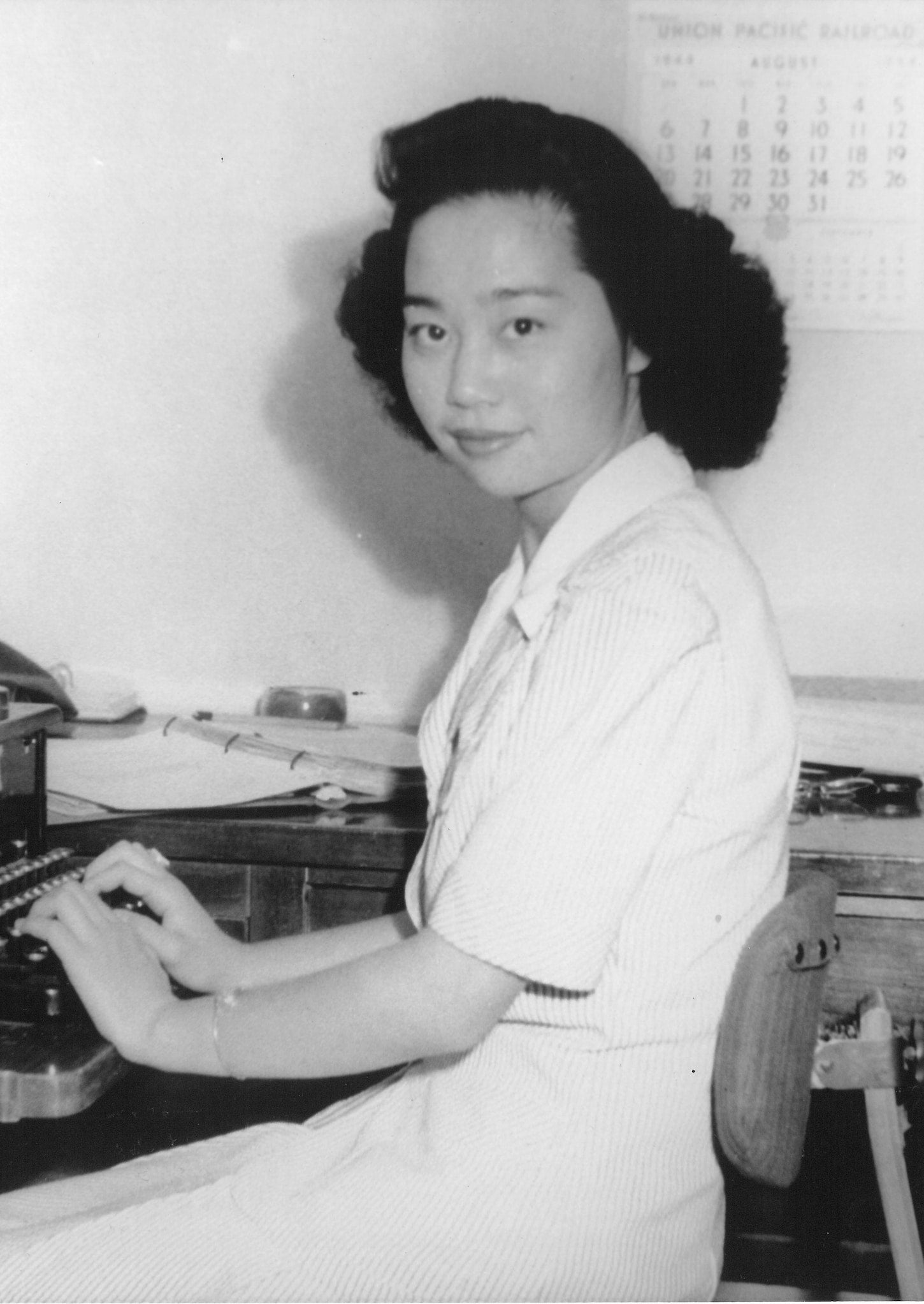 Japanese American activist Mitsuye Endo sitting at a typewriter, turns to the camera.