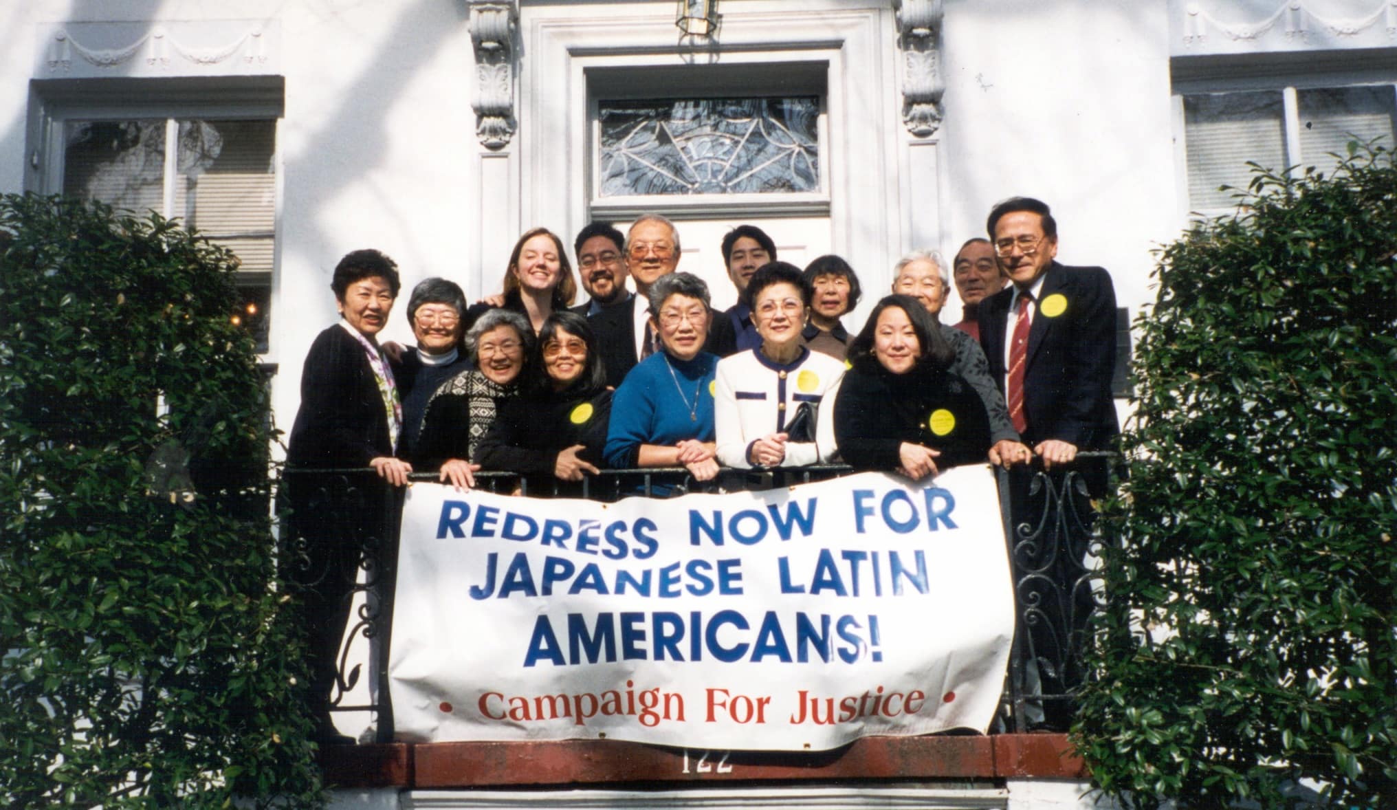 A group of people holding up a banner with the words "REDRESS NOW FOR JAPANESE LATIN AMERICANS: CAMPAIGN FOR JUSTICE."
