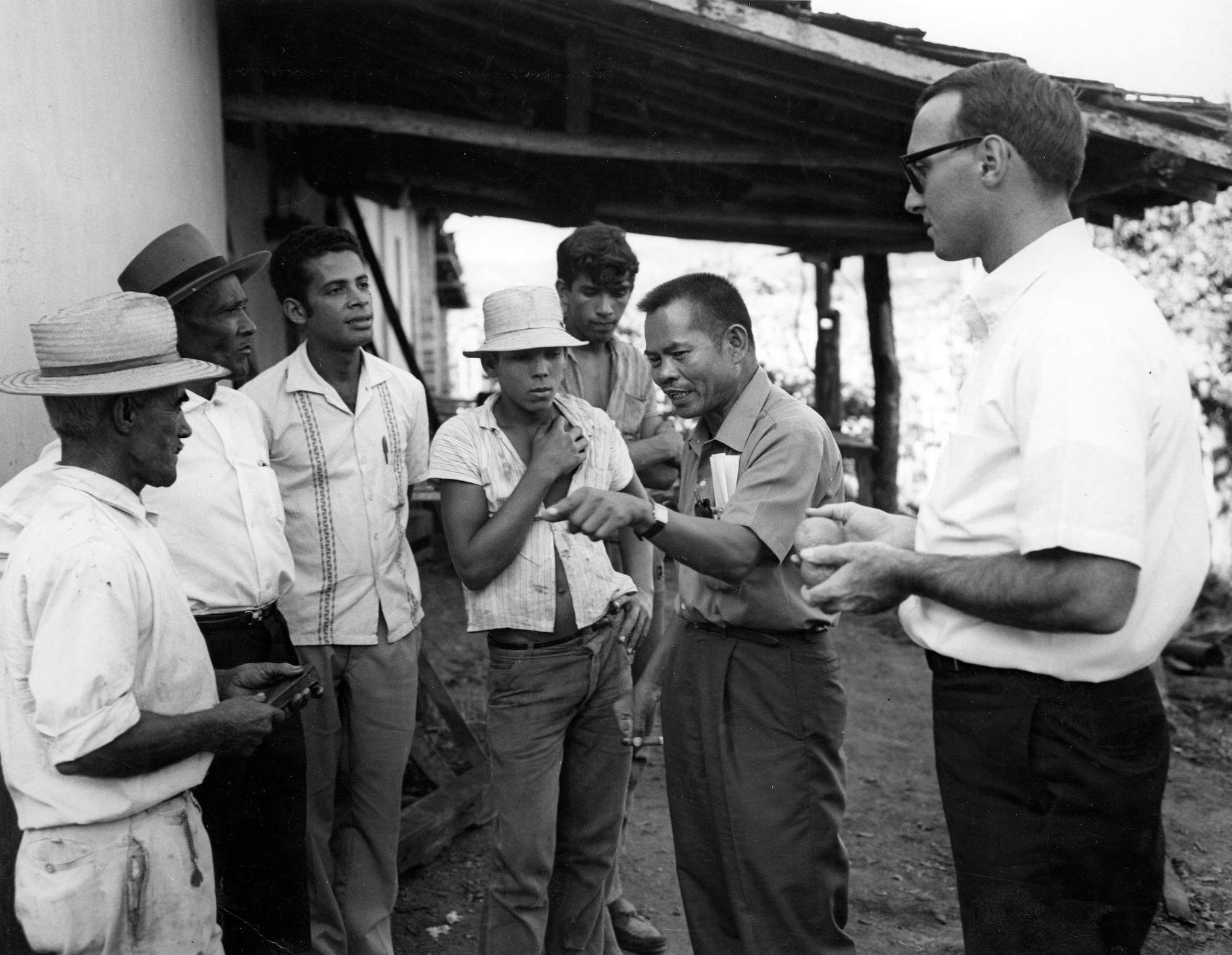 Larry Itliong and Dick Ginnold speaks to a group of Brazilian farm workers in front of a building.