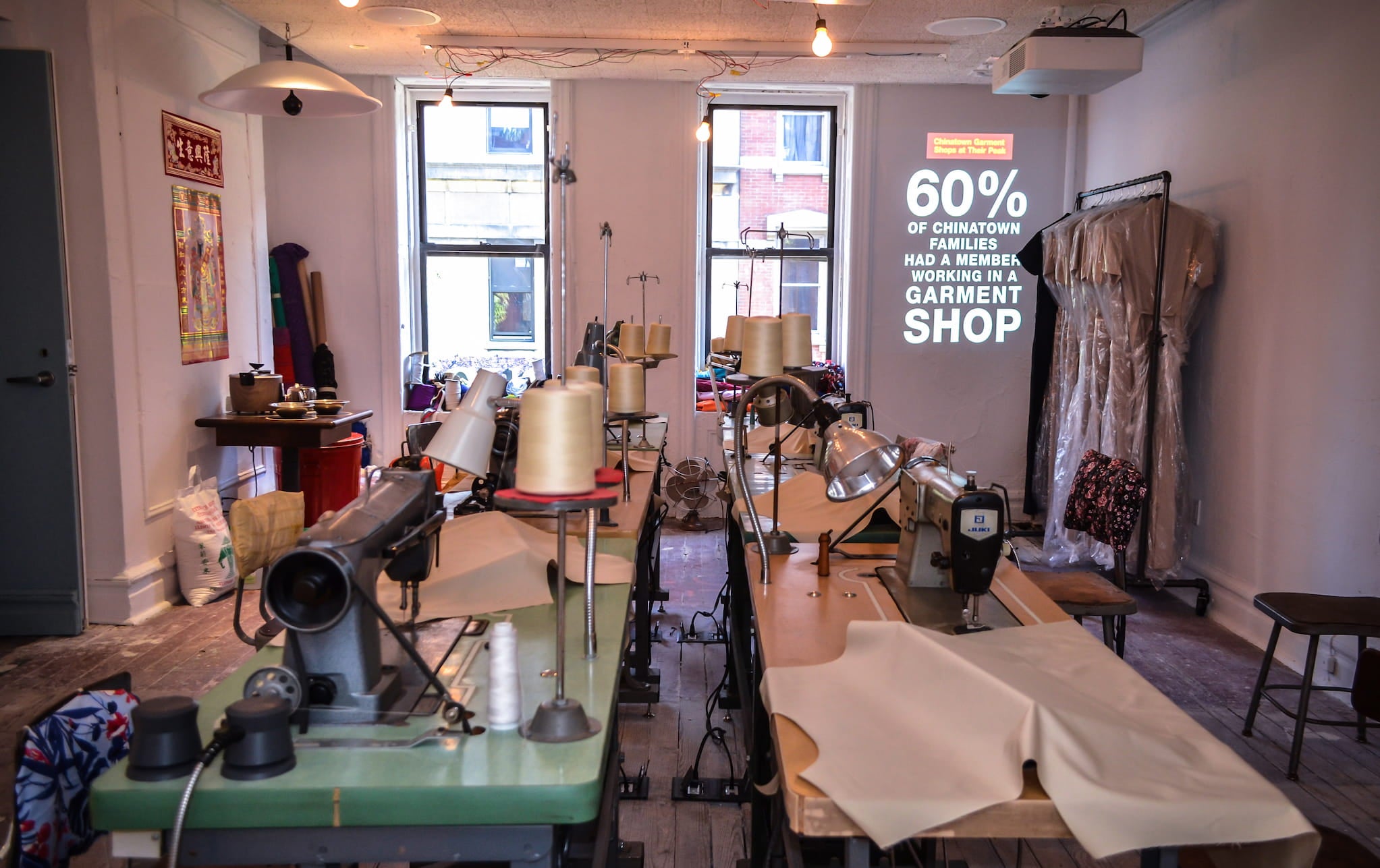 Museum exhibit depicts a typical sewing factory from the 1980s, showing a small room with multiple tables, sewing machines, and clothing racks.